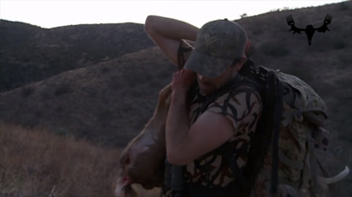 Hunter carrying deer quarter over shoulder in dry hills with MeatEater logo overlay