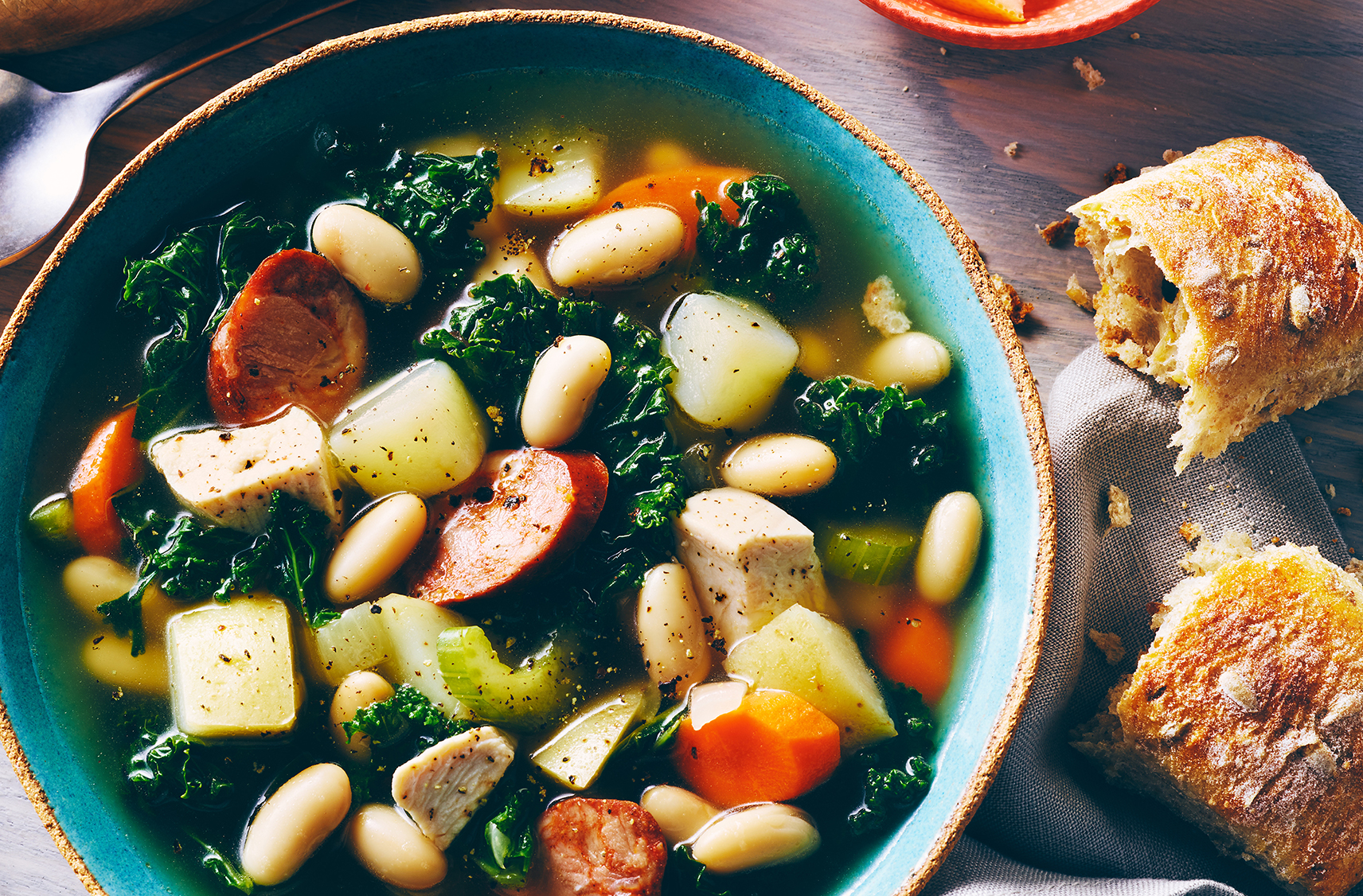 A soup of kale, chorizo, white beans, celery and potato in a clear broth