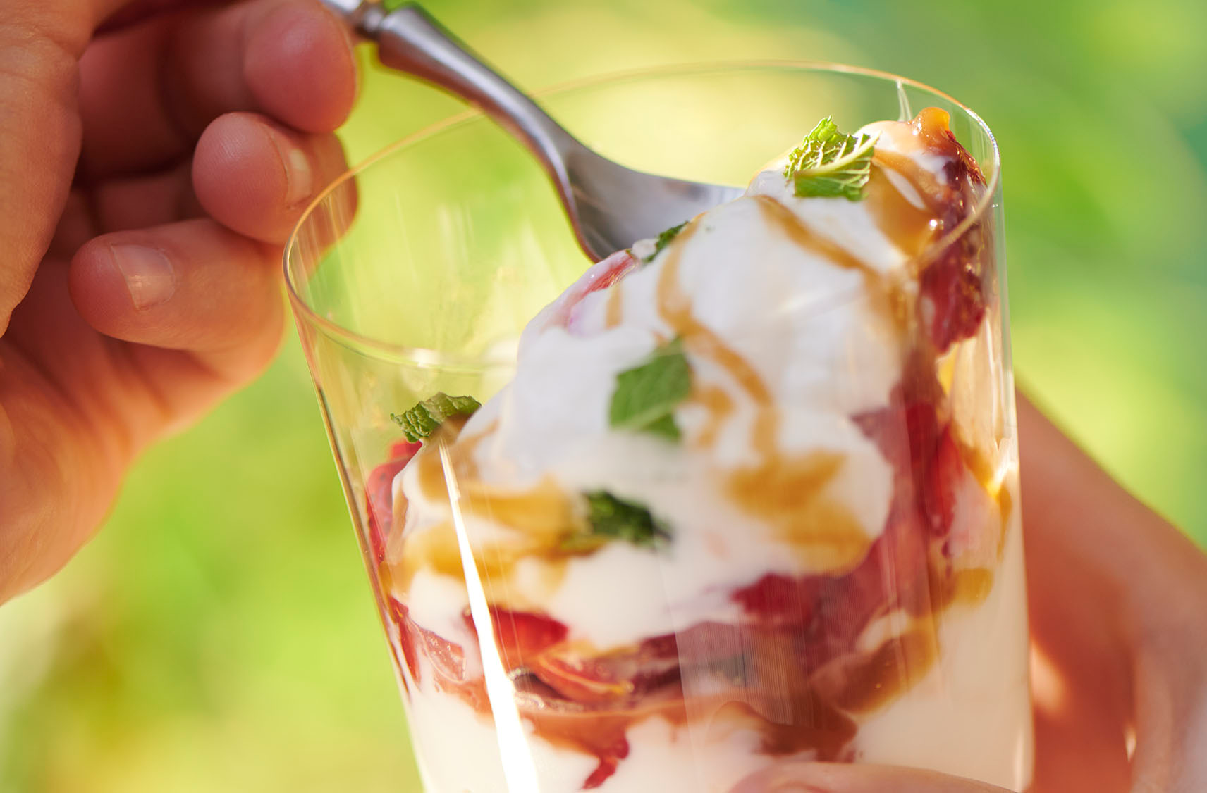 A cup of tangy plain skyr yogurt with a strawberry sauce, maple caramel drizzle  and pieces of freshly chopped mint, in hand ready to be enjoyed. 