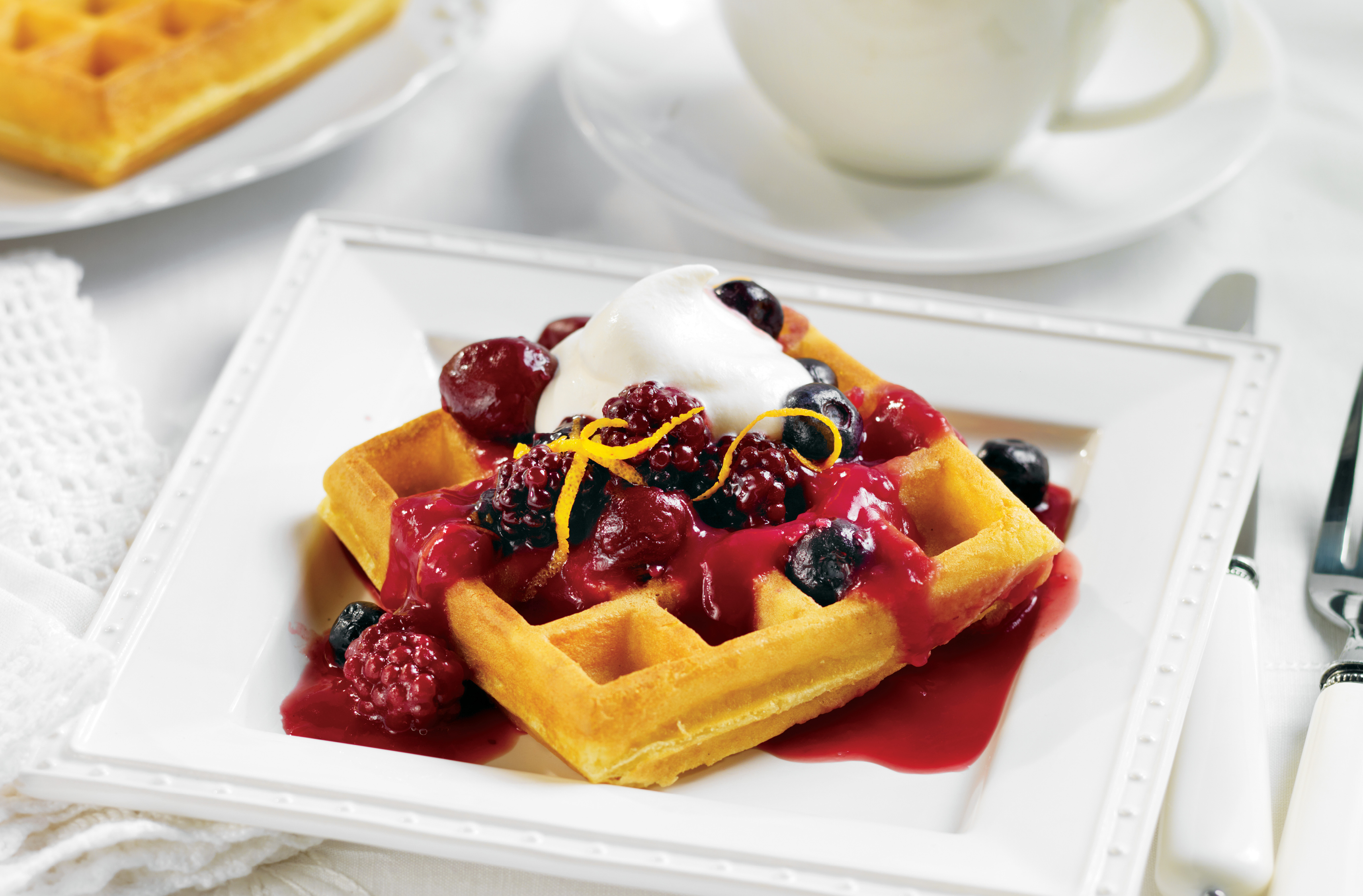 A square waffle on a plate topped with a power fruit blend & whipped cream
