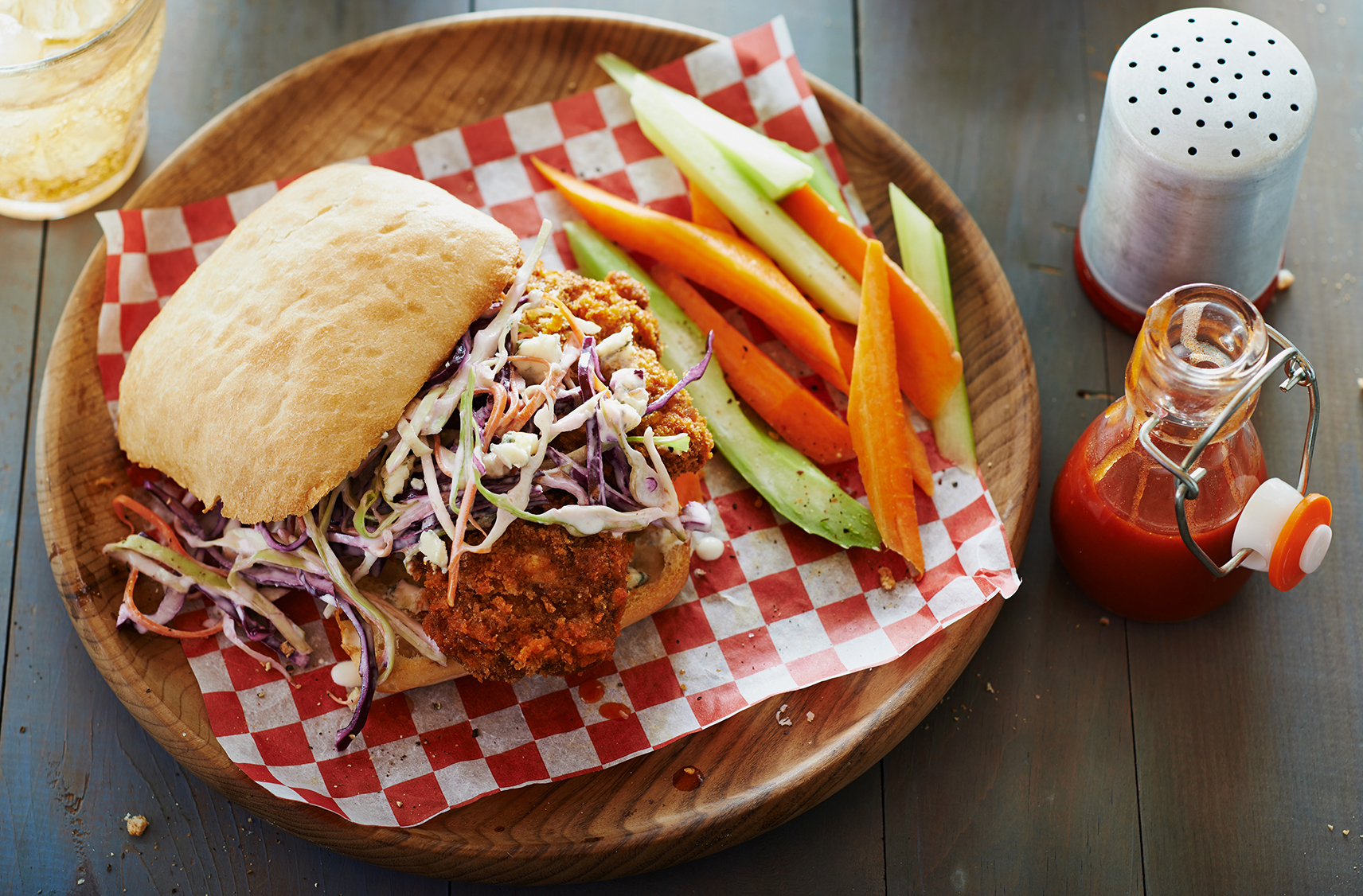 A crispy chicken sandwich on a ciabatta bun with coleslaw by carrot sticks