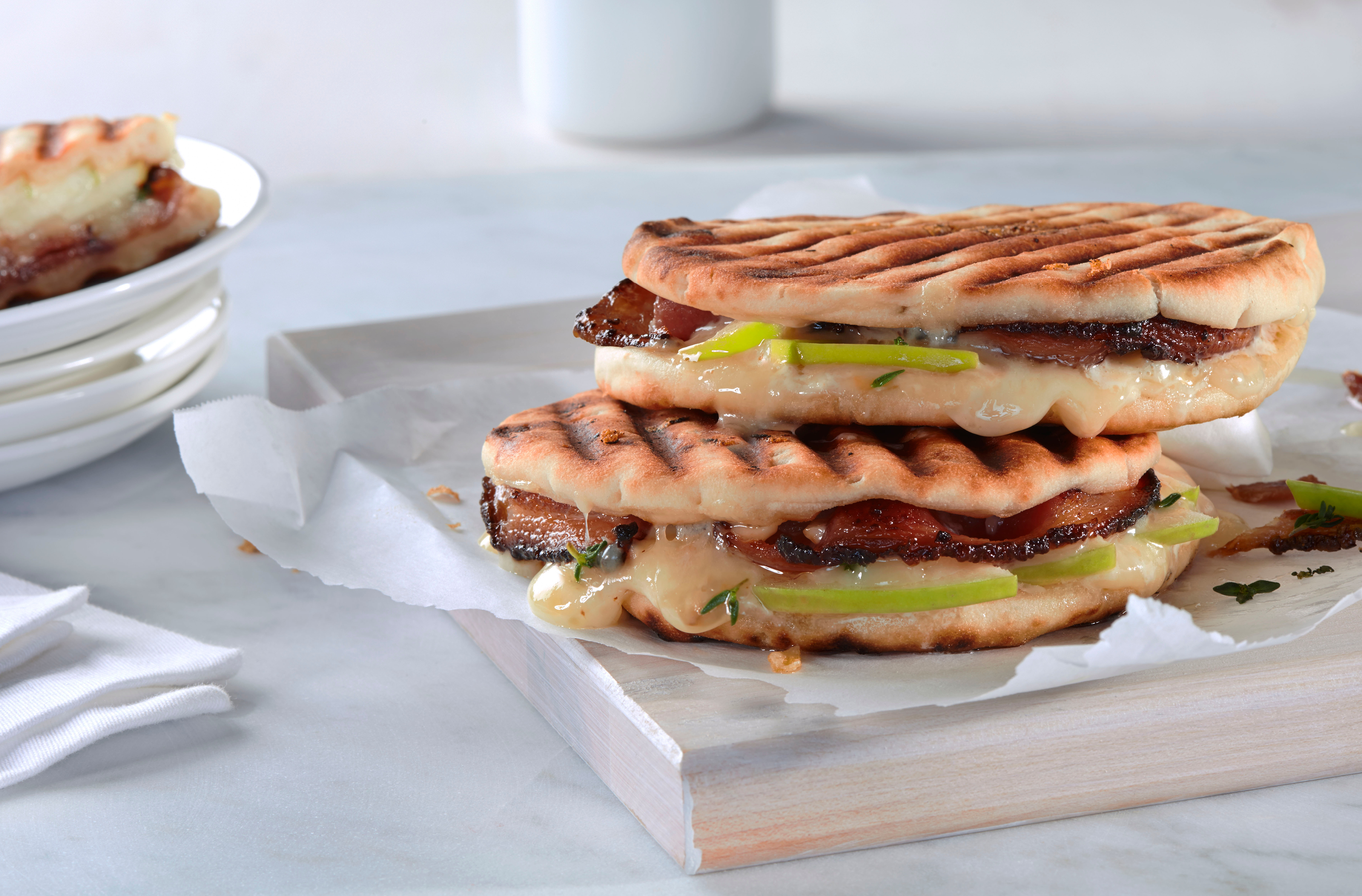 2 grilled naan sandwiches filled wiith bacon, melted cheese, green apple
