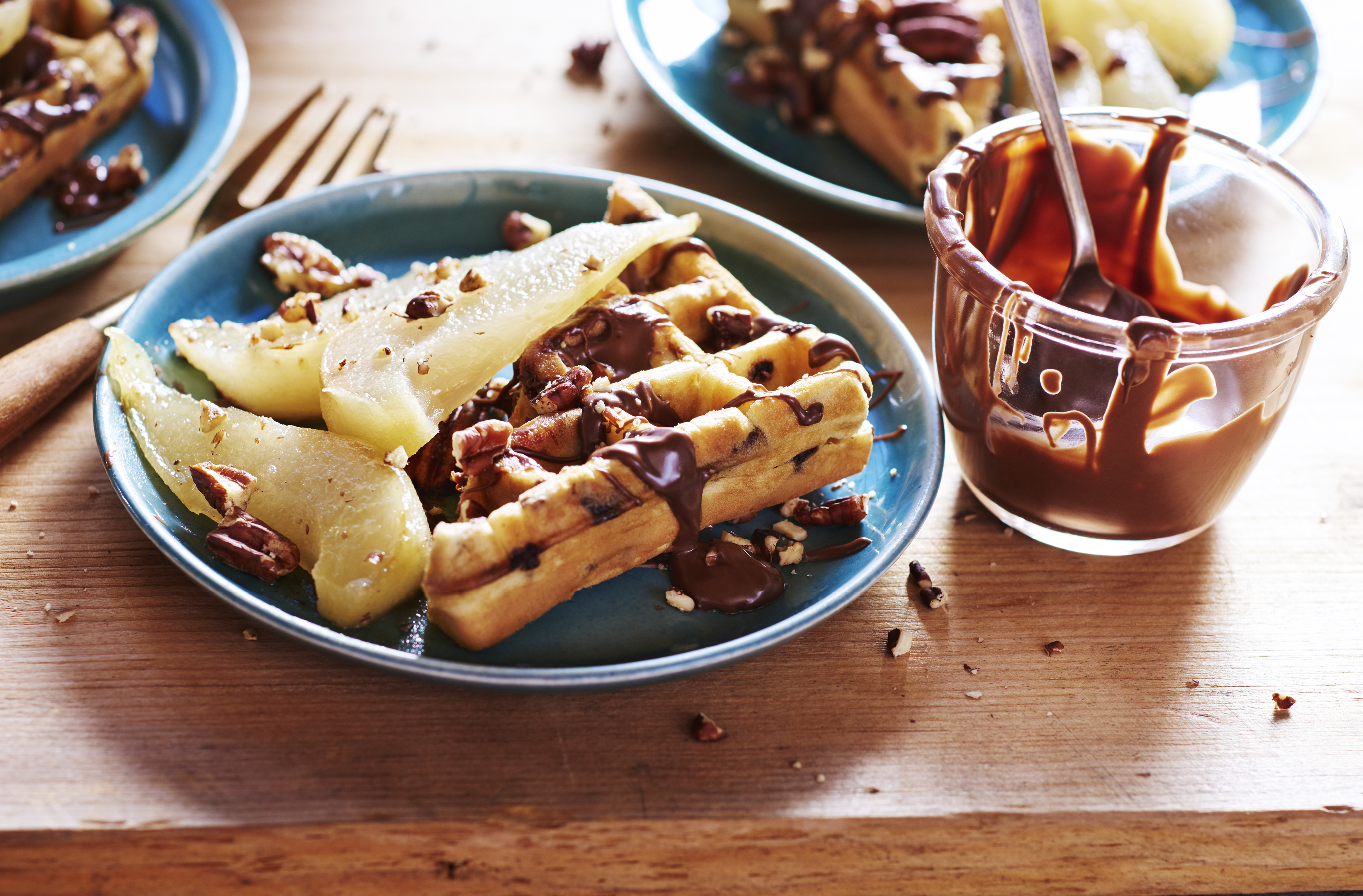 Sur une assiette, une gaufre aux brisures de chocolat garnie de tranches de poire, de noix et de chocolat
