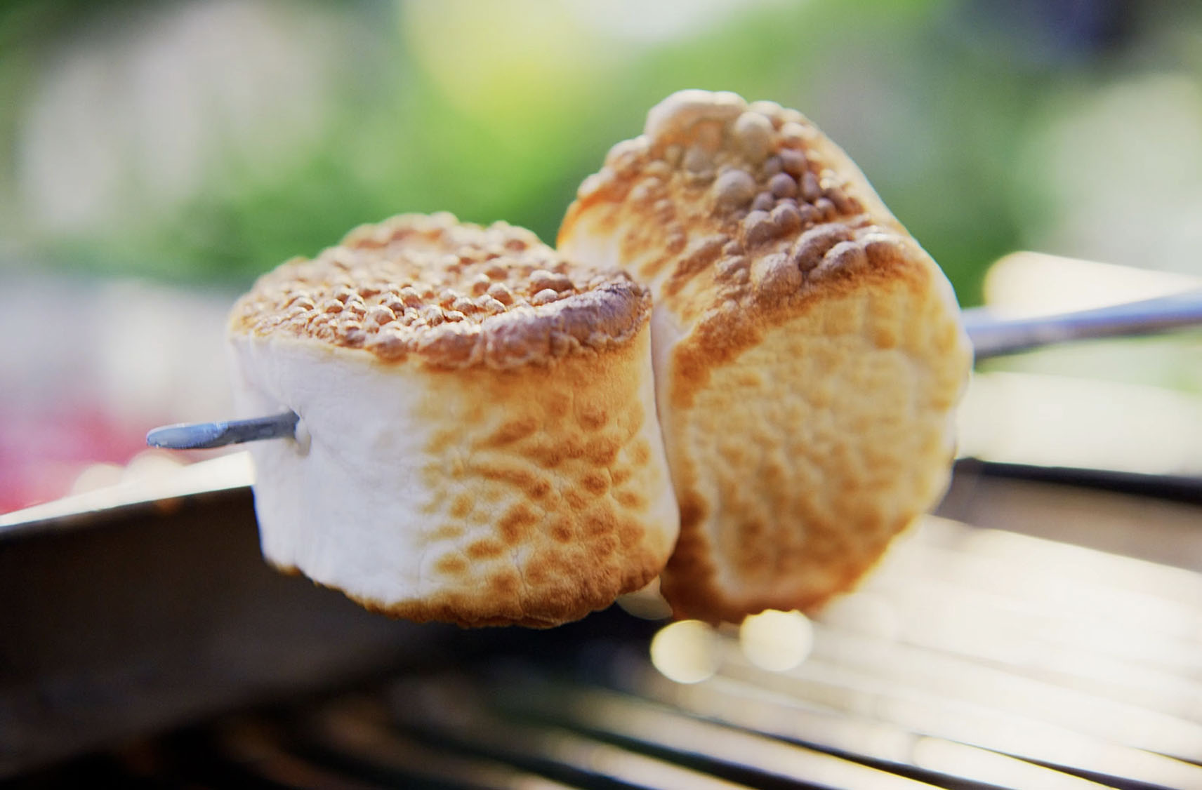 Two golden roasted marshmallows on a skewer over a grill