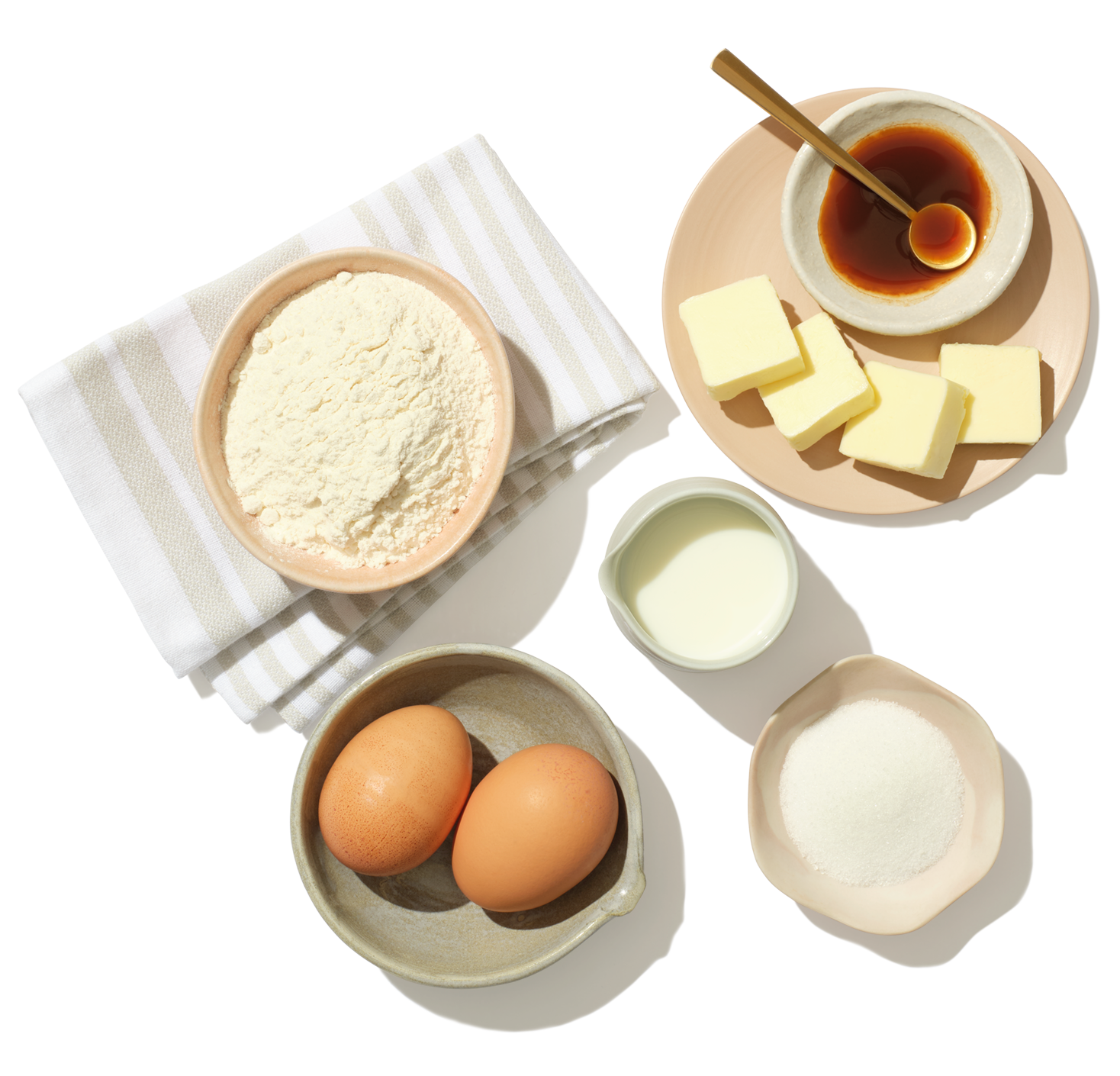 Several bowls with pre-measured ingredients sits on a table top including eggs, sugar, butter, flour and milk.