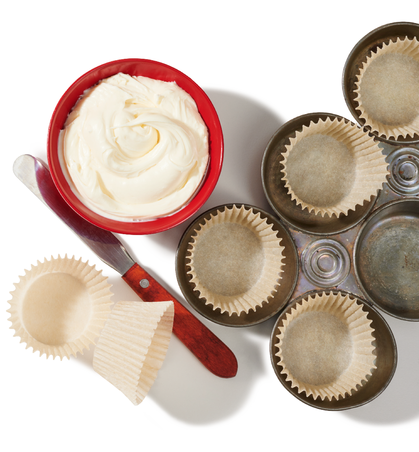 Empty muffin cups and making tins sit next to a bowl of cream cheese frosting