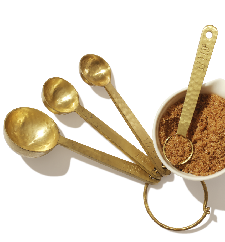 Un petit bol de cassonade repose sur une surface à côté de cuillères à mesurer dorées avec une cuillère à thé mesurée de cassonade dans le bol