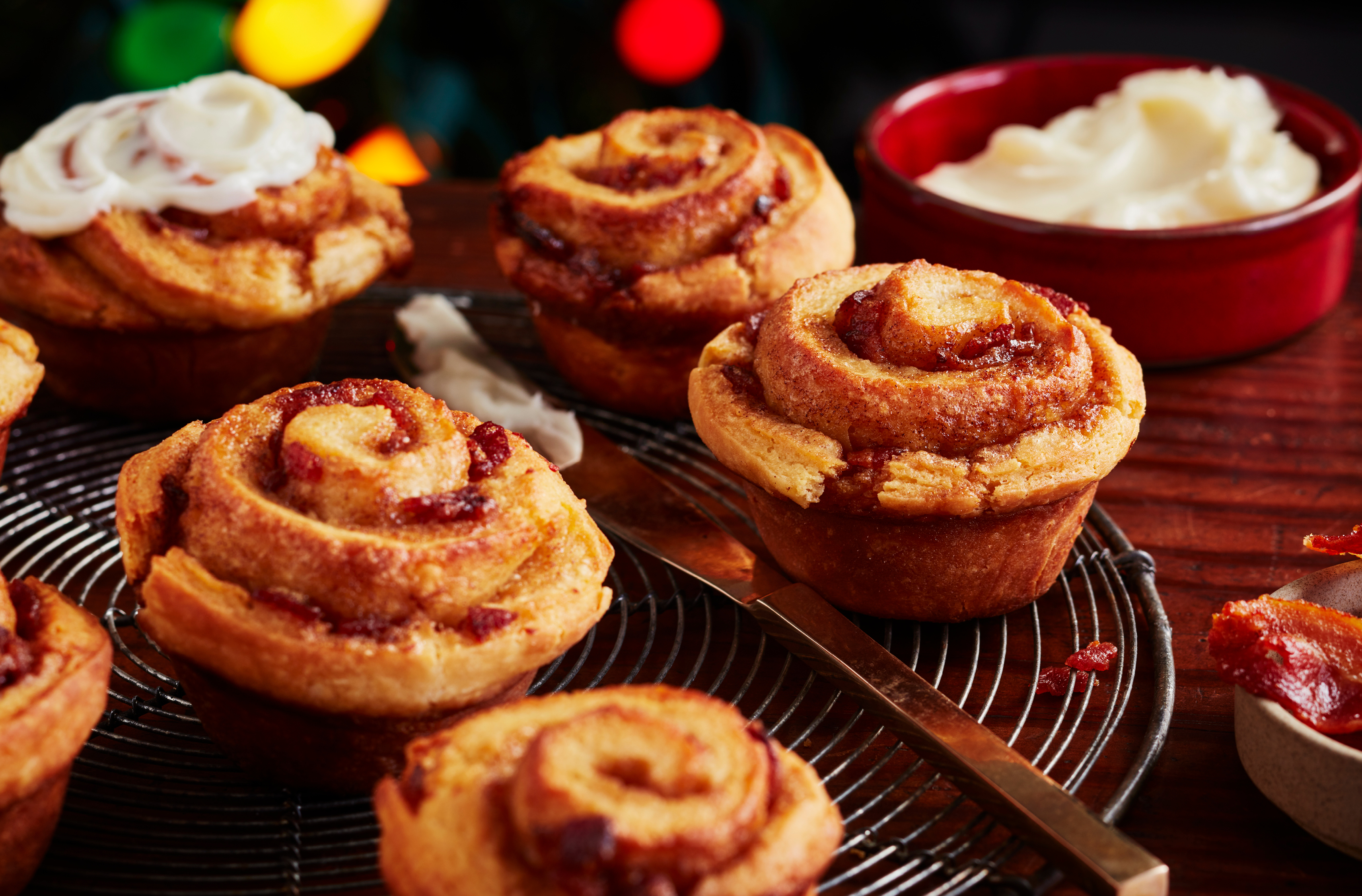 Cinnamon rolls, one topped with icing, cool on a wire rack beside a knife
