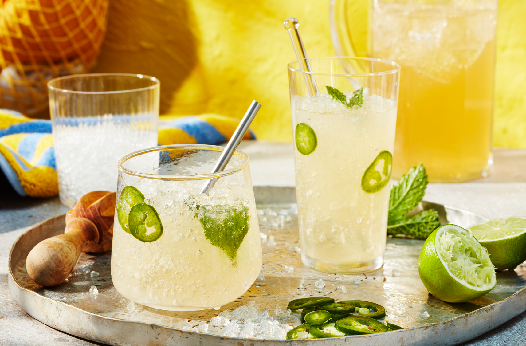 Deux verres de cocktail au citron et au gingembre décorés de lime, de menthe et de tranches de jalapeno placés sur un grand plateau.