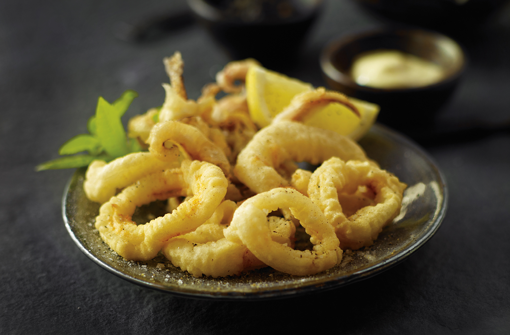 A plate of battered, fried calamari, with a lemon wedge