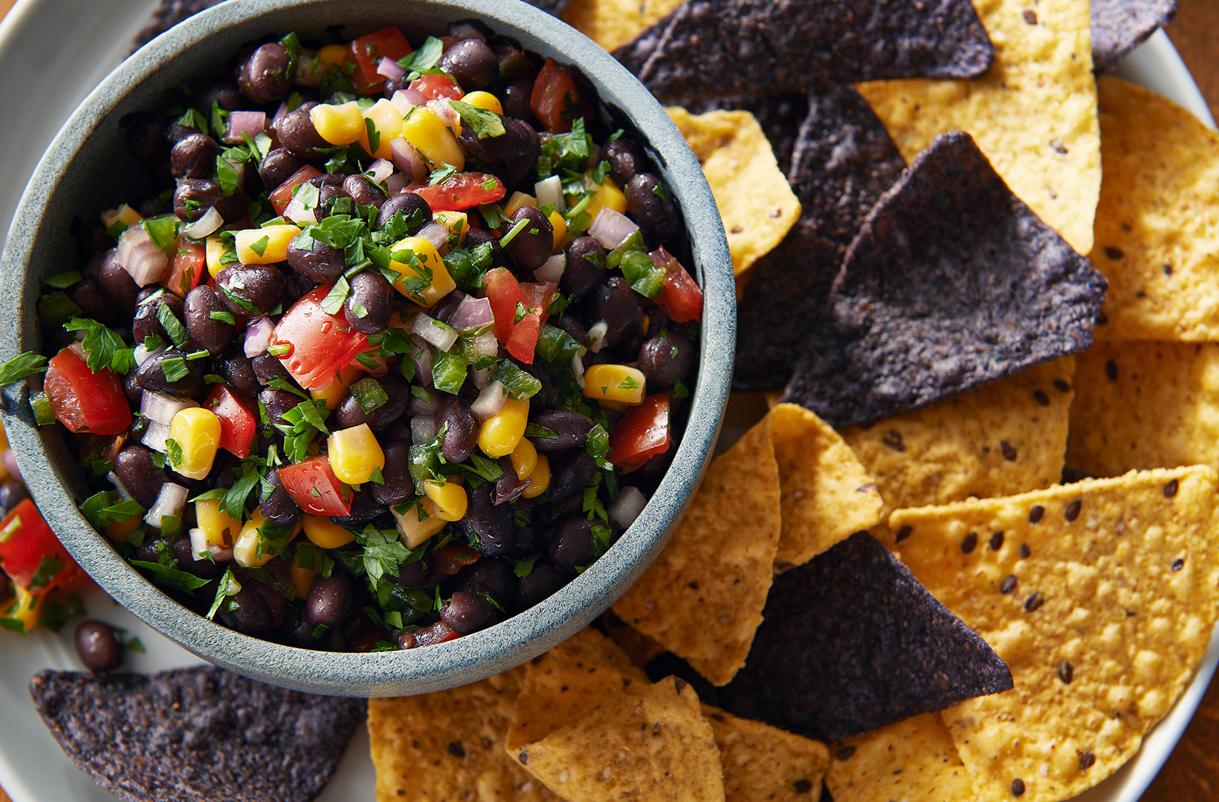 A bowl filled with a corn and Black Bean Salsa on a larger tray of yellow and blue corn tortillas