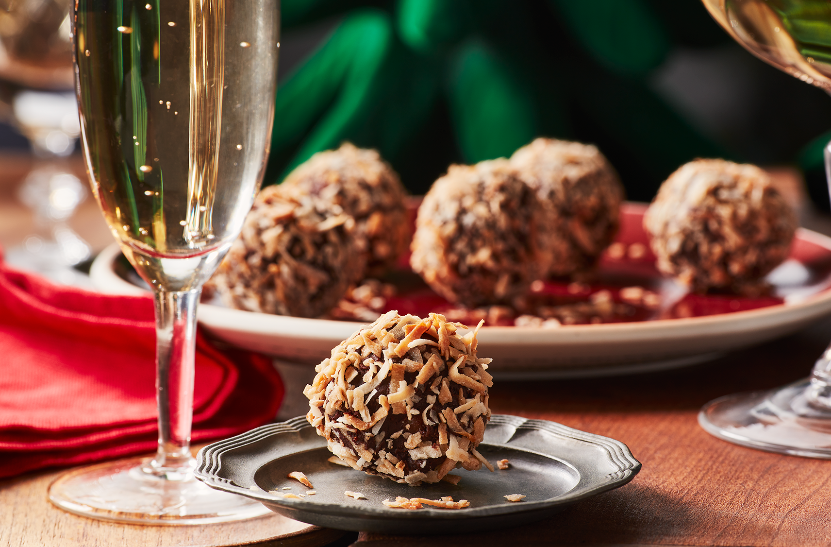 Une petite soucoupe avec une truffe végétalienne au chocolat et à la mangue devant une assiette remplie de truffes, à côté d'un verre de boisson pétillante.