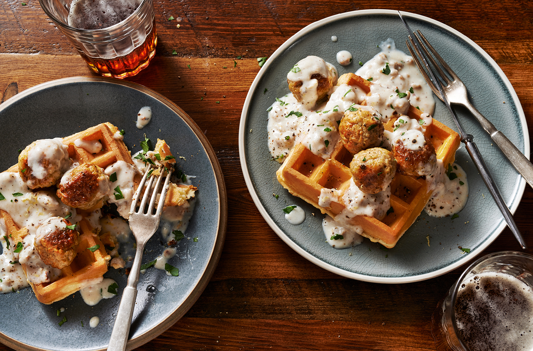 Two plates of waffles topped with chicken meatballs and gravy 
