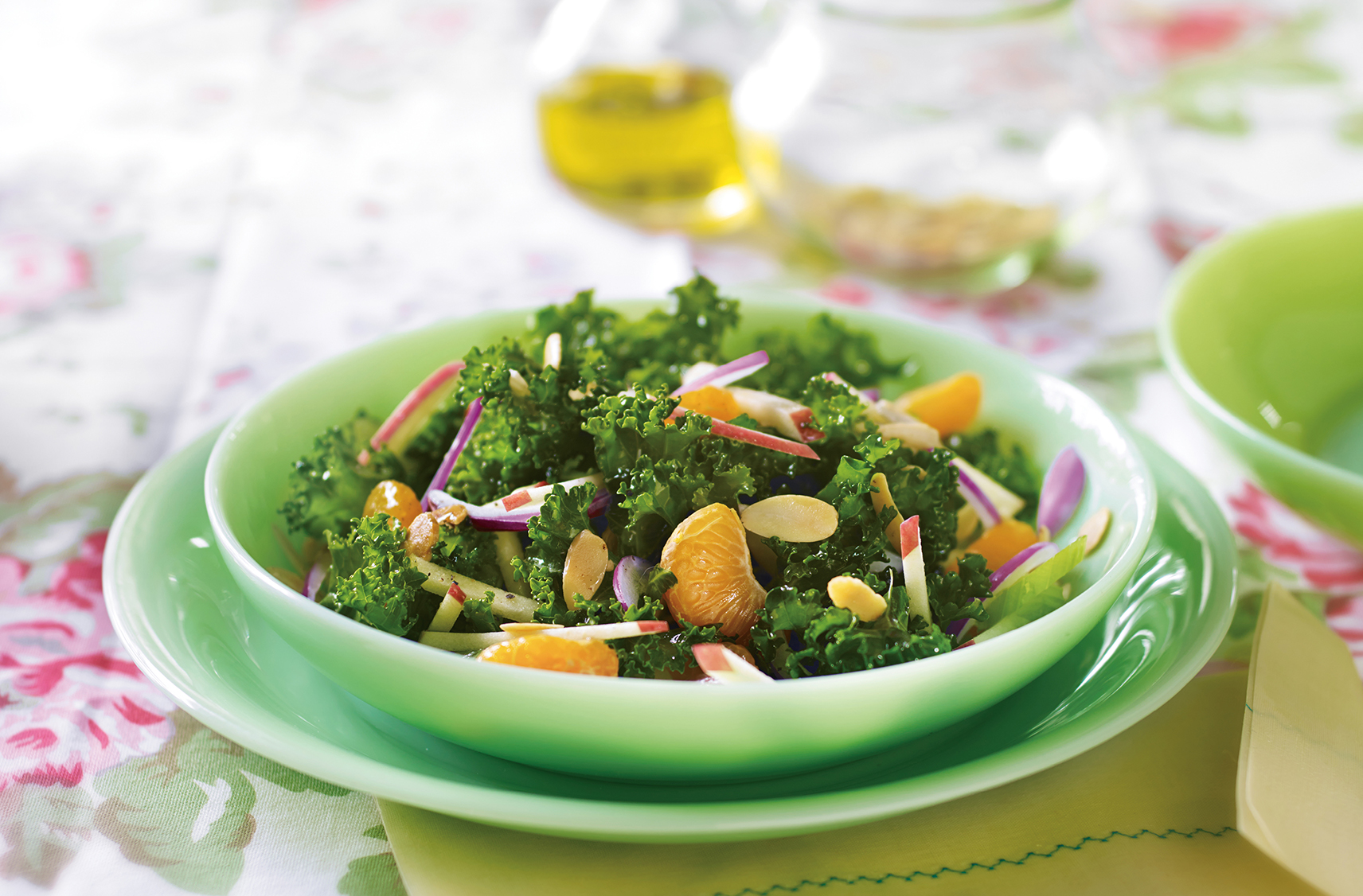 A salad bowl sitting on a lunch sized plate with a salad containing kale and mandarin oranges.