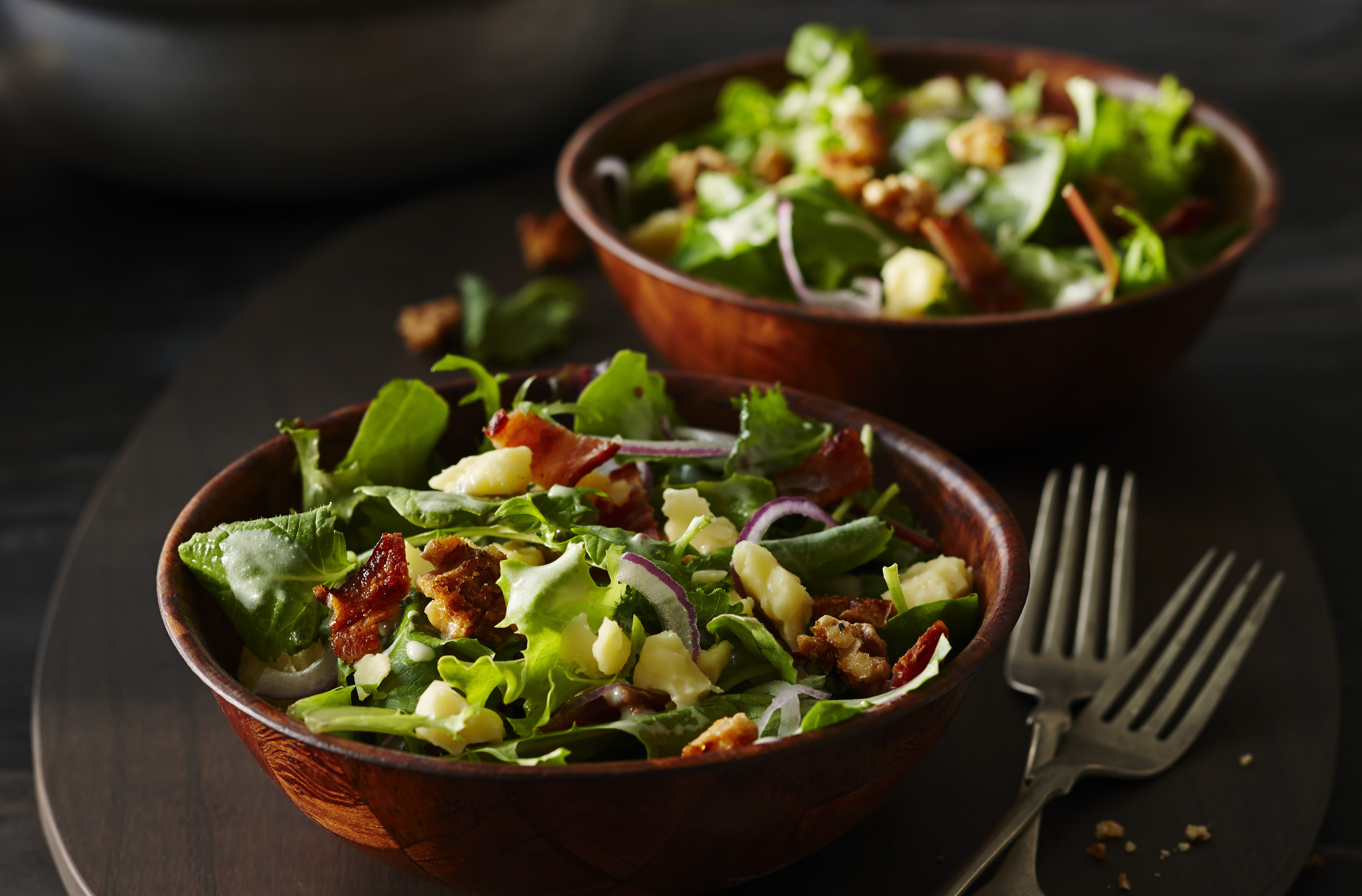 Une salade de légumes-feuilles garnie de cheddar Isle of Man, de tranches d'oignon rouge et de bacon servie dans de petits bols à salade en bois