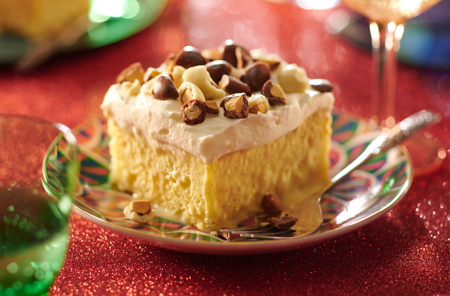 A slice of cake with whipped icing and topped with pieces of chocolate-covered almonds on a festive plate.