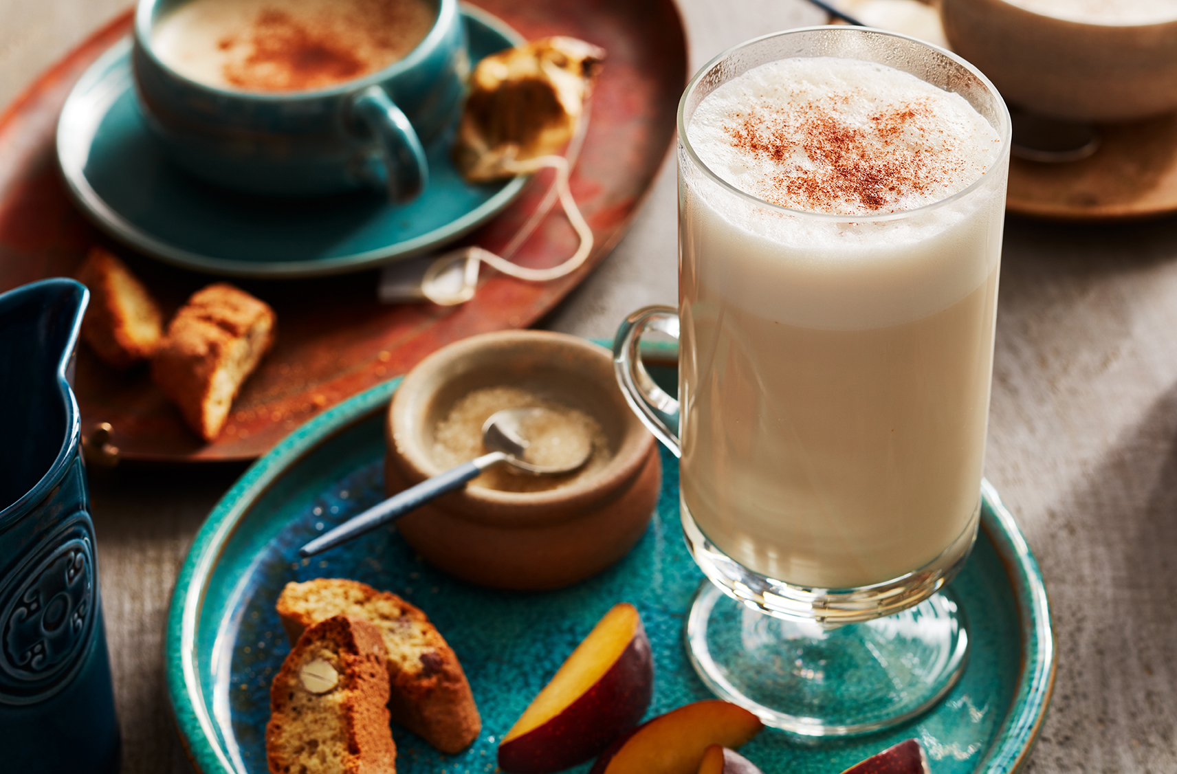 A glass of dirty chai latte served with biscotti and nectarine slices