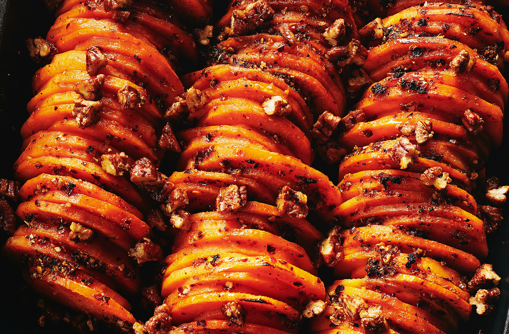 rows of maple pecan spiced sweet potatoes all thinly sliced and placed inside a baking dish.  sprinkled with chopped pecans