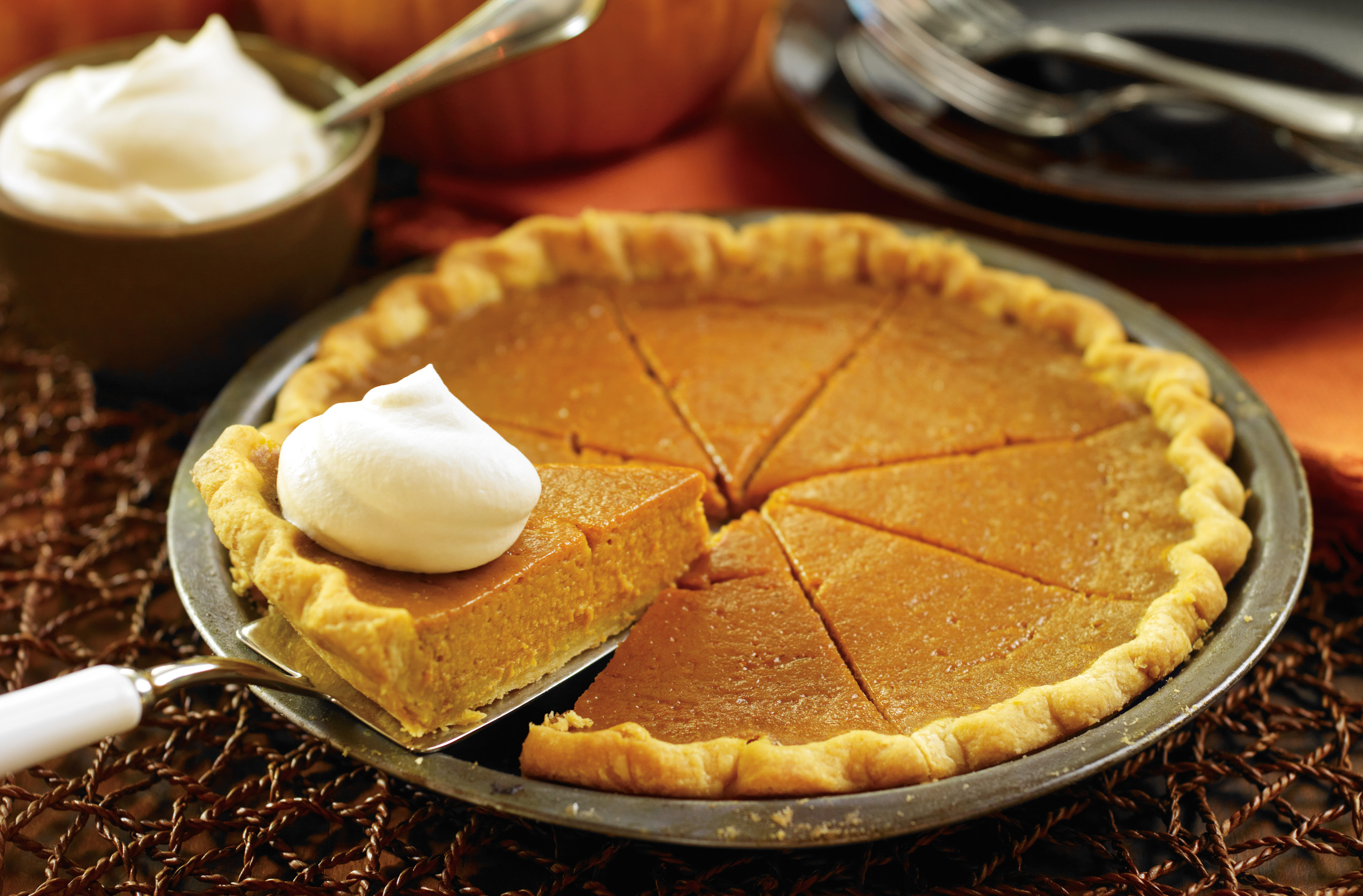 A pumpkin pie in a pie tin with 1 whipped cream topped slice being removed
