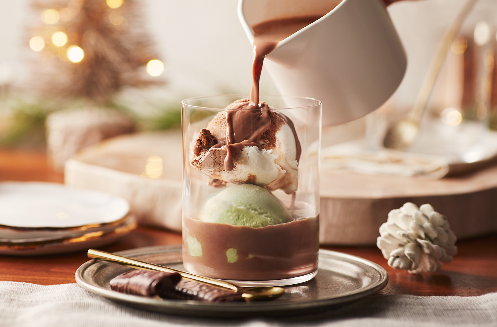 Du chocolat chaud à la menthe en train d'être versé sur deux boules de crème glacée à la menthe poivrée et à la vanille dans un verre.