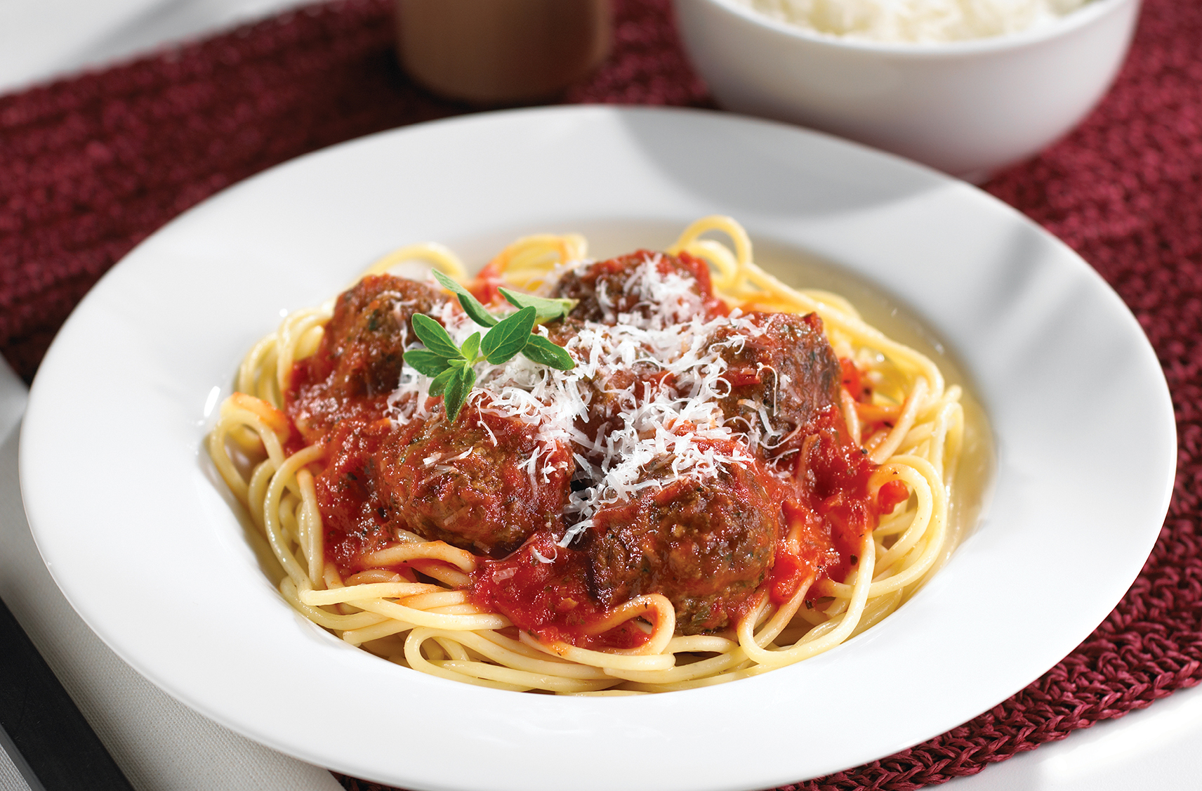 A dinner sized plate with meatballs and marinara on top of spaghetti noodles topped with Parmesan beside a small bowl of Parmesan cheese.