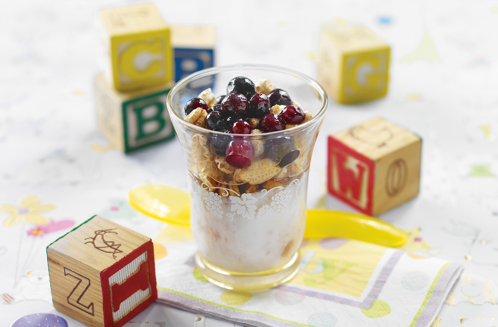 Juice glass of yogurt topped with cereal & berries  
