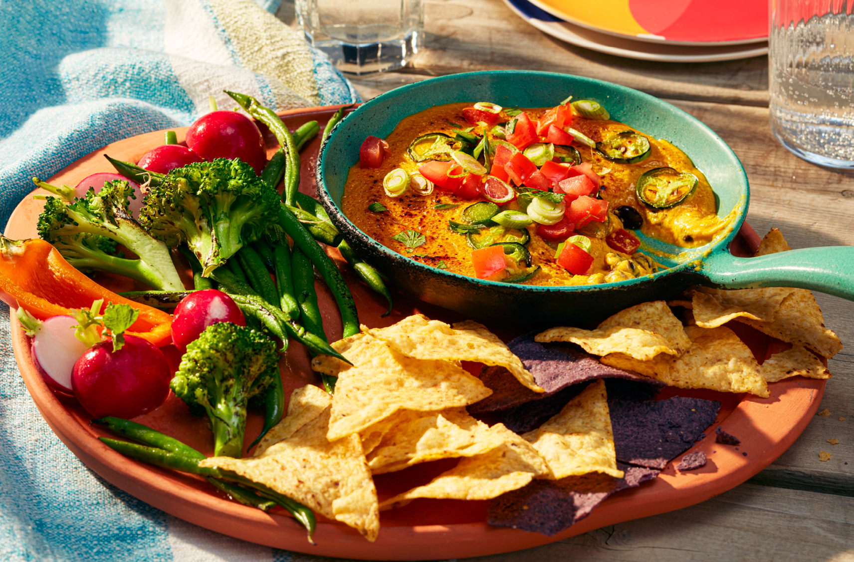 A serving tray filled with veggies, broccoli, tomatoes, sliced peppers and a side bowl filled with a Vegan Southwest Queso-Style Dip