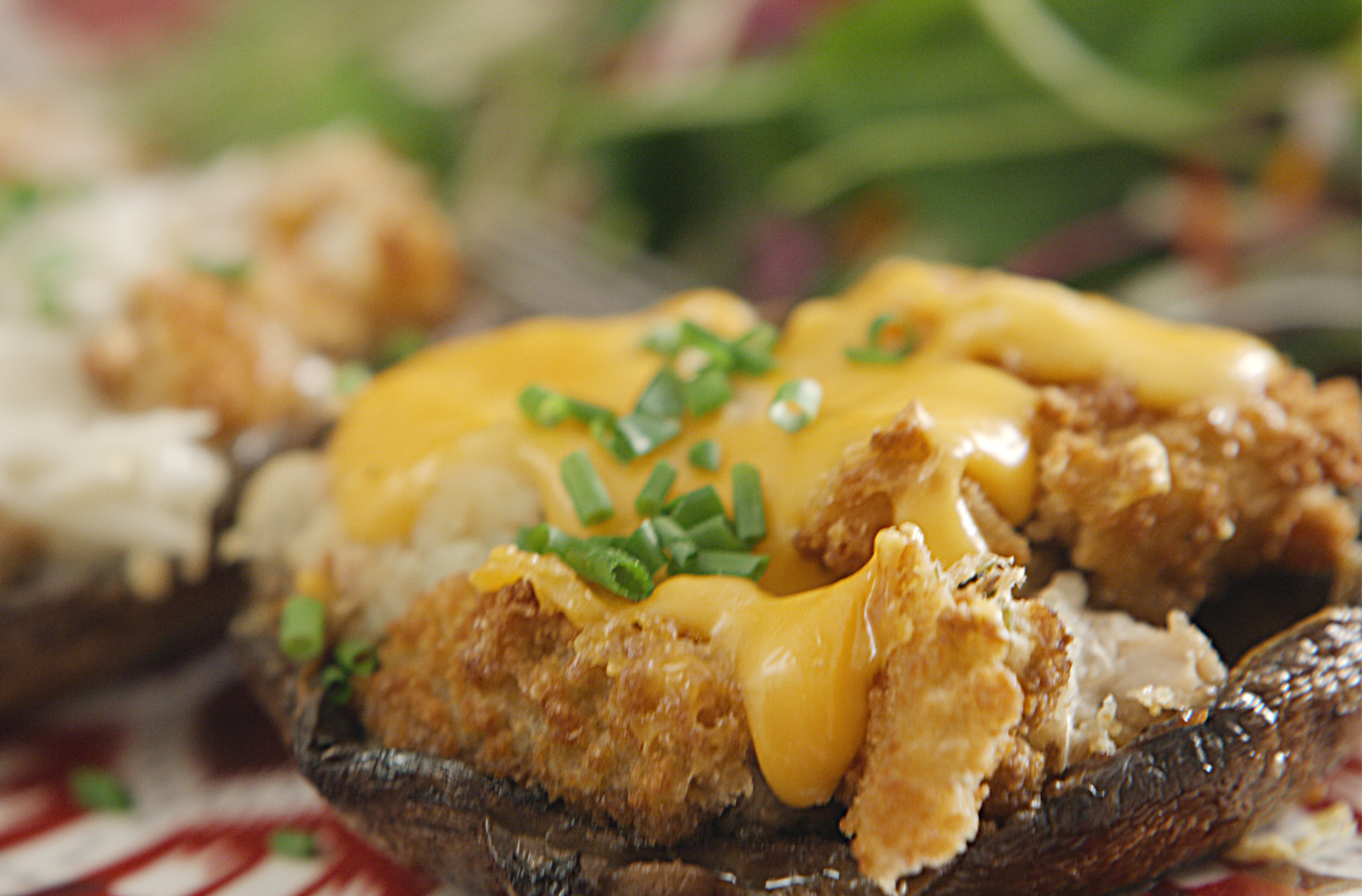 Close up image of a plant-based stuffed portobello muschroom cap topped with a dairy free cheese sauce and chives.