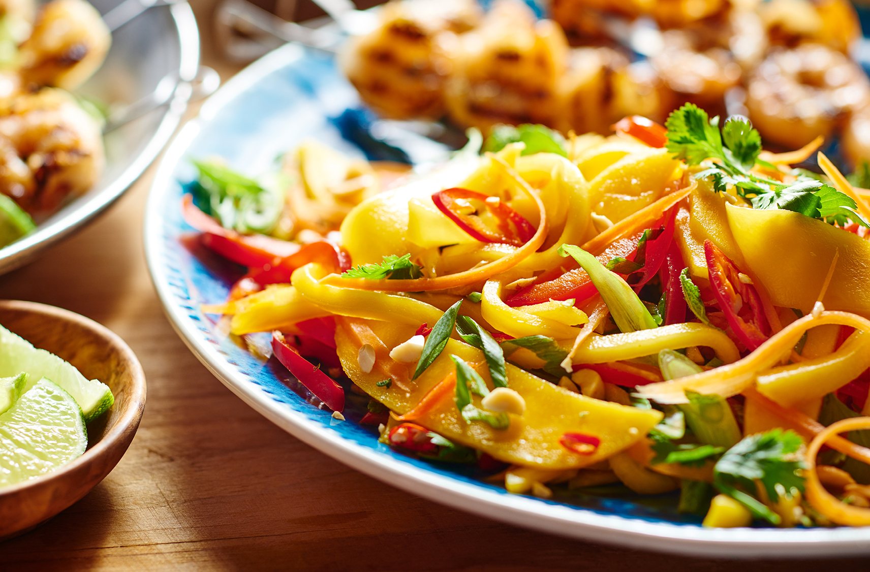 A plate of thai mango salad and shrimp skewers on a wooden table
