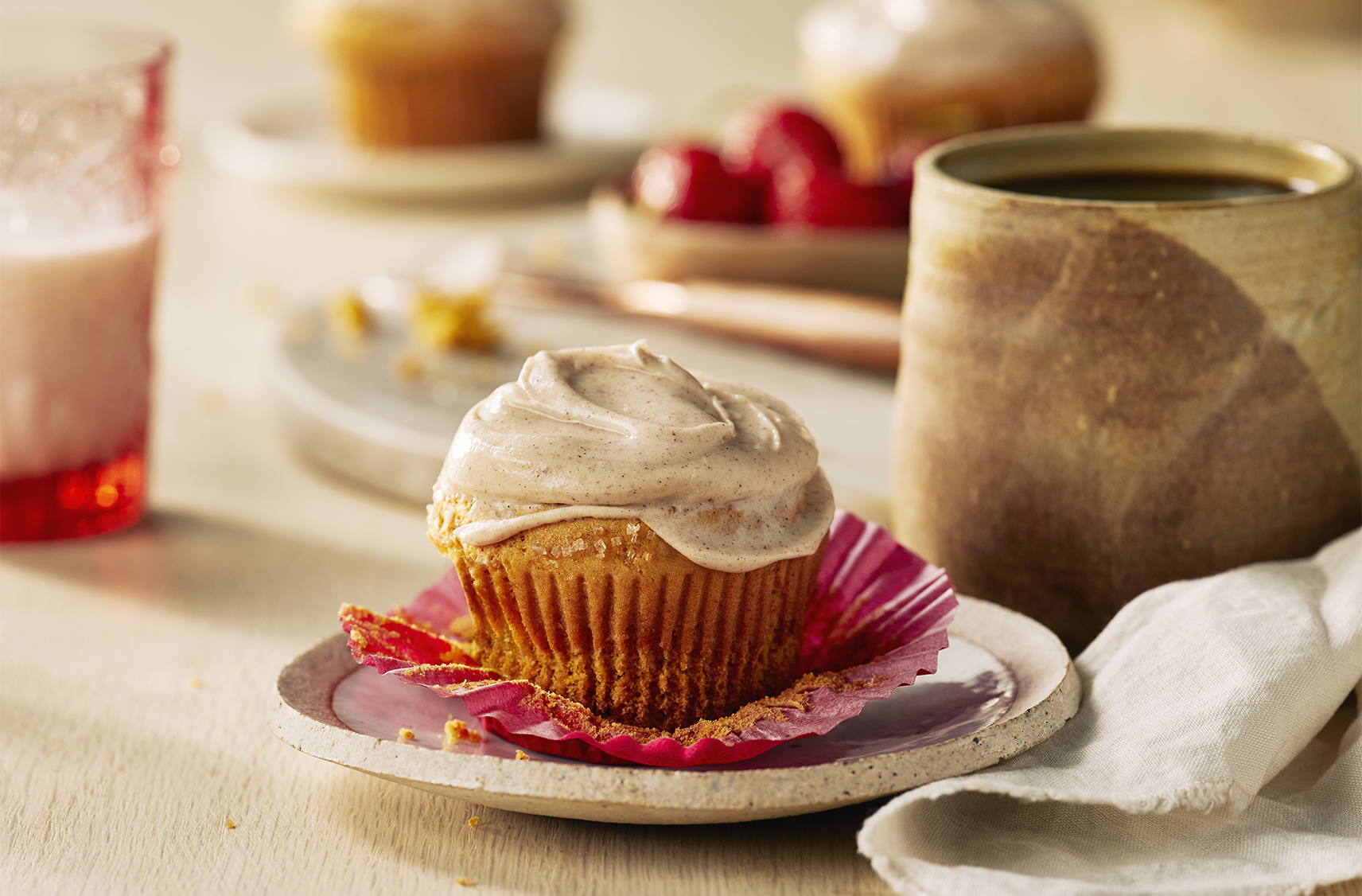 A saucer with a pumpkin spice muffin on it topped with a cream cheese spread next to a hot beverage and two more plates of the same.