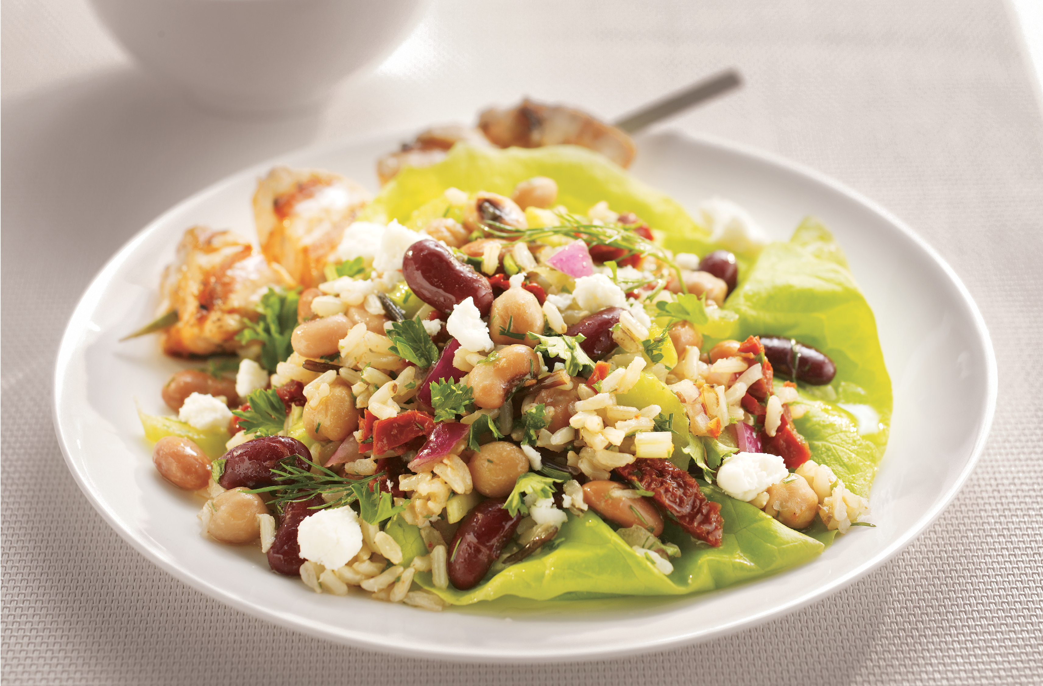 Une salade de riz brun, de riz sauvage et de légumineuses avec féta et une brochette de poulet sur une assiette
