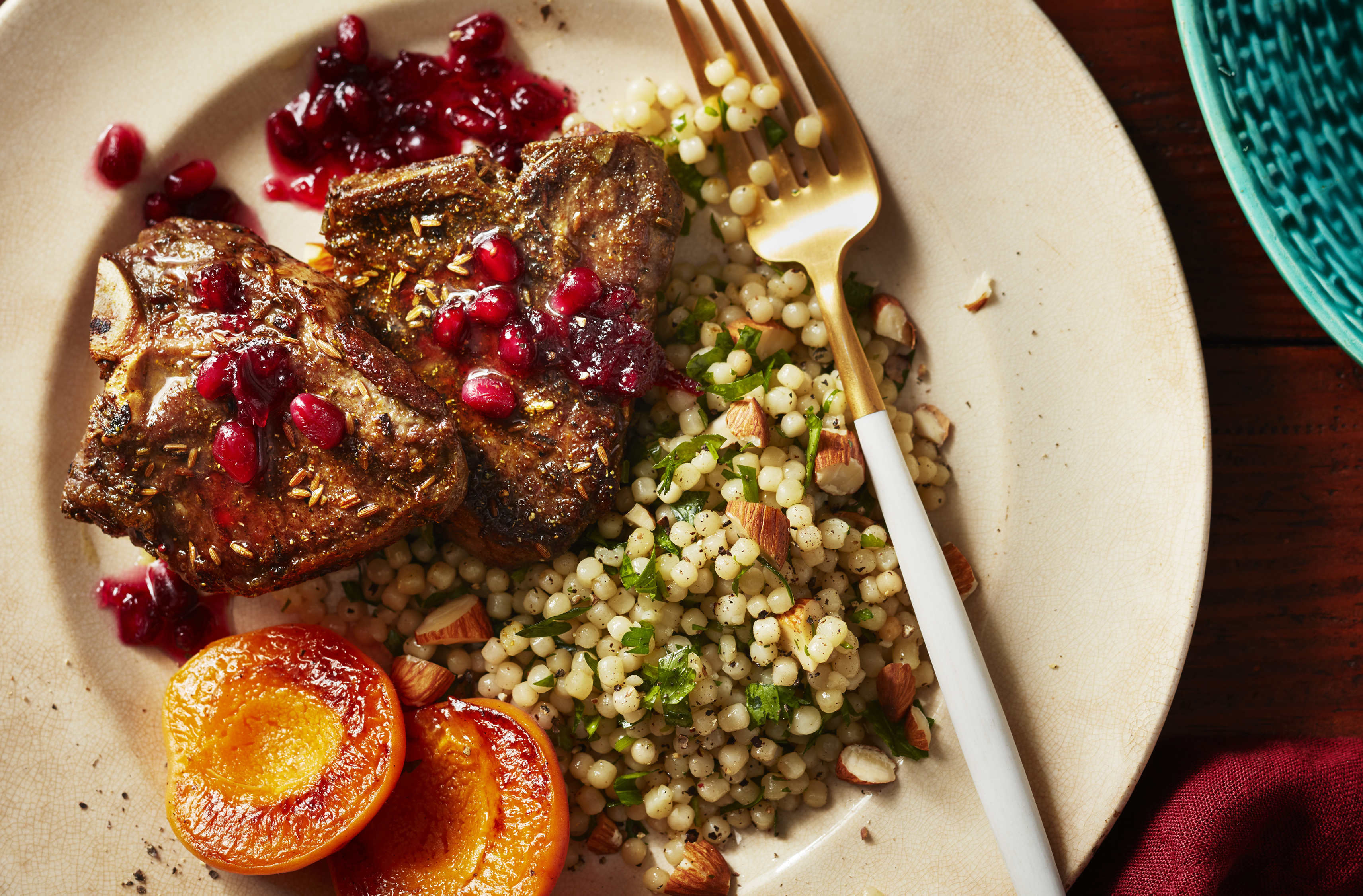 Une sauce à la grenade nappe des côtelettes d'agneau à côté de pêches et d'une salade de couscous israélien
