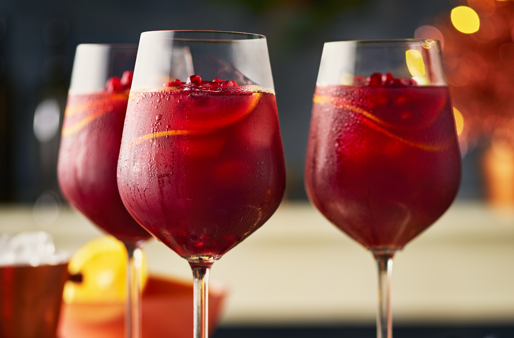 Three glasses of sangria garnished with orange slices and pomegranate anils