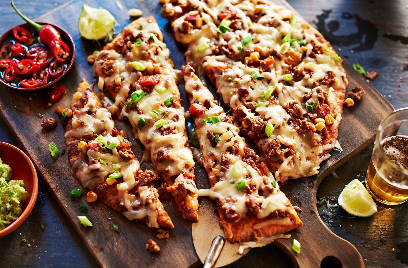 A sliced Mexicasa pizza with cheese, green onions, peppers & ground meat