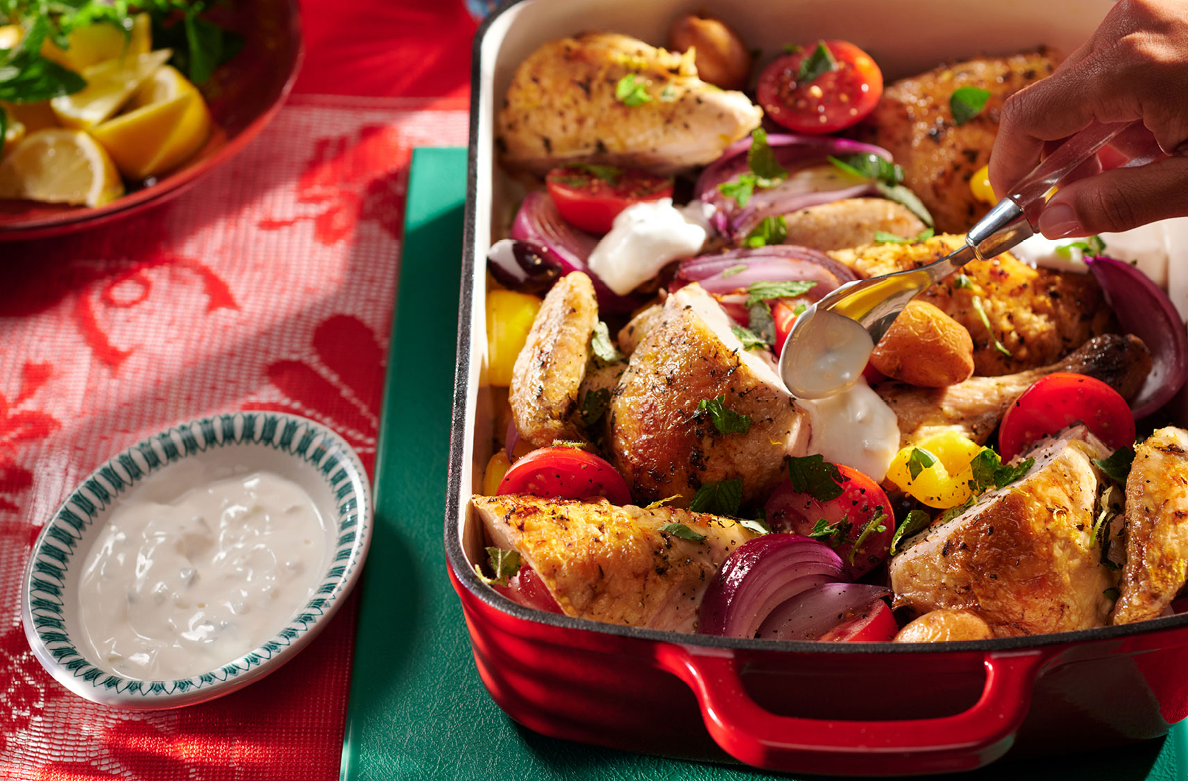 Une rôtissoire émaillée remplie de gros morceaux de poulet rôtis avec des morceaux de tomates, de pommes de terre, d'oignons et de poivrons.