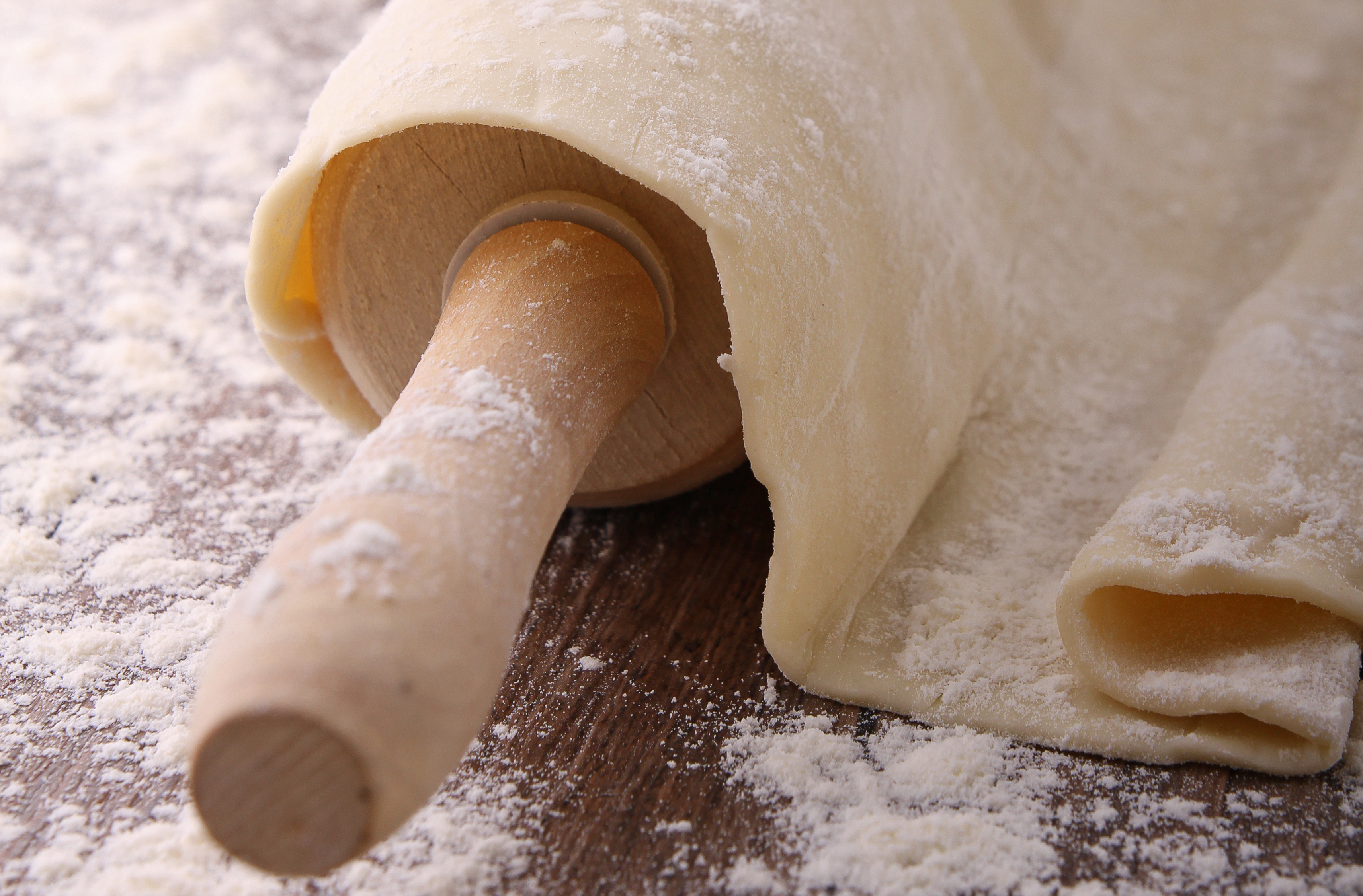 Une pâte à pizza amincie, enroulée autour d’un rouleau à pâtisserie en bois