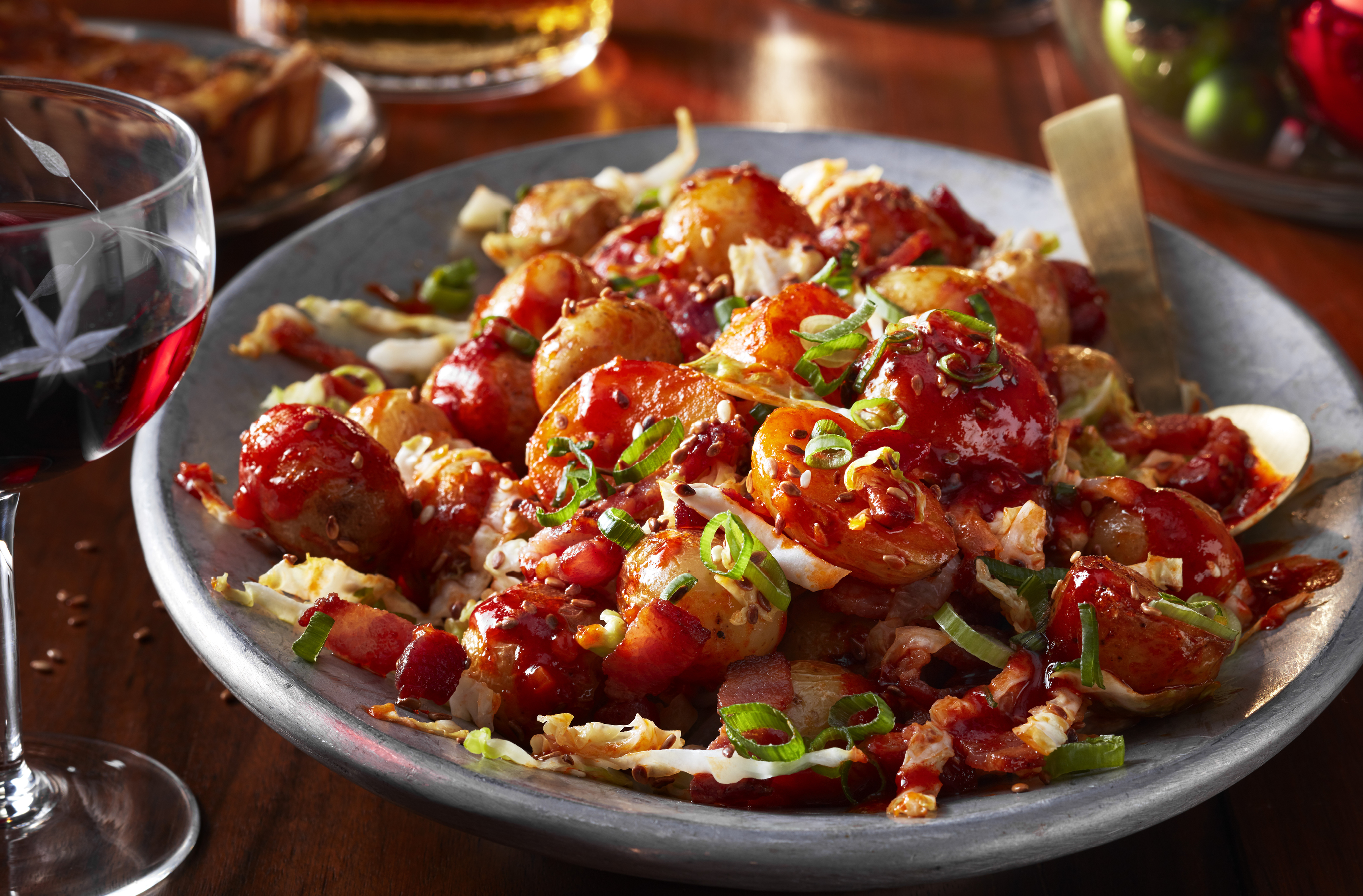 A platter of korean fried potatoes topped with bacon and scallions 
