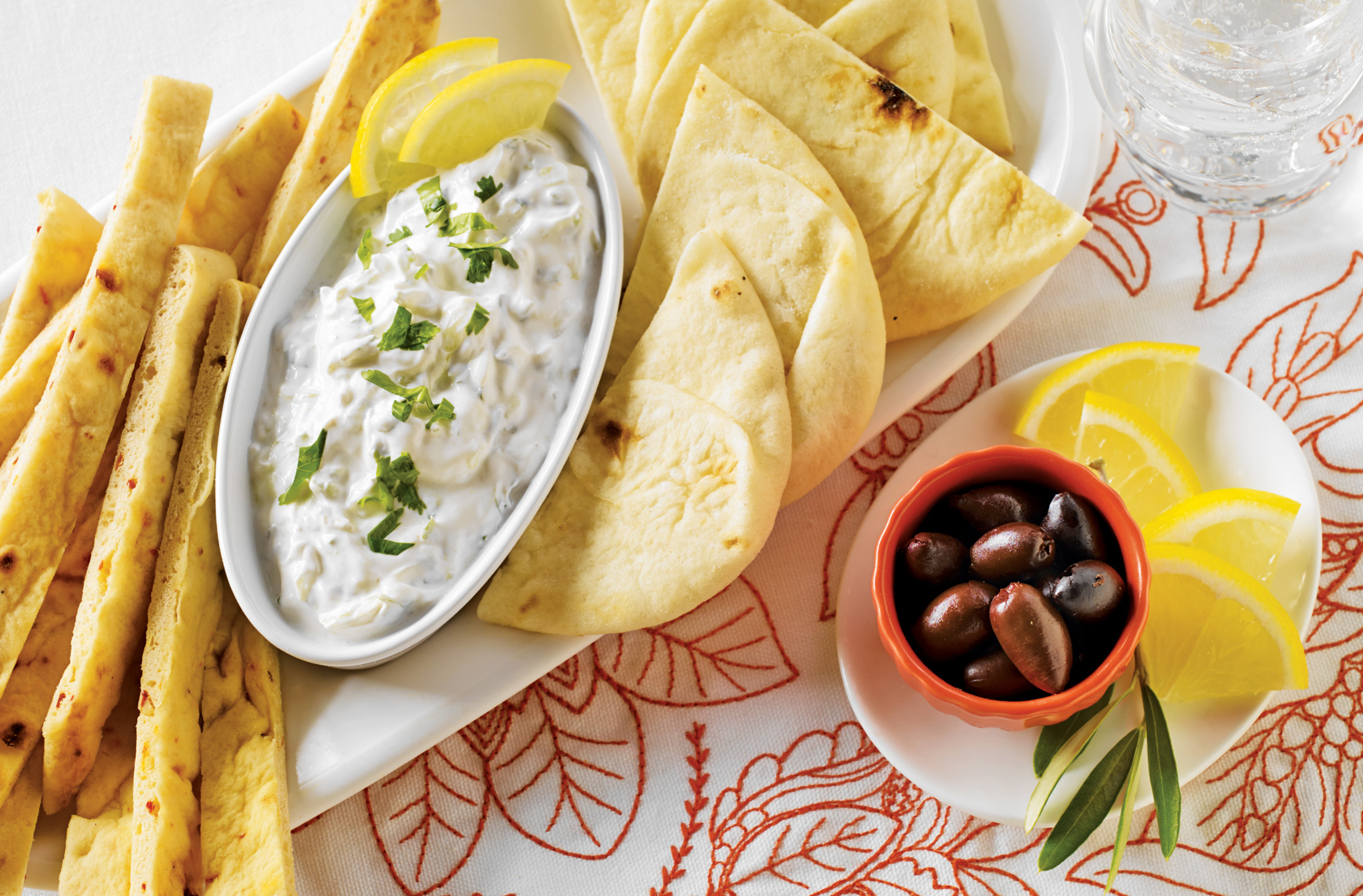 A bowl of raita yogurt & cucumber dip on a tray with pieces of naan
