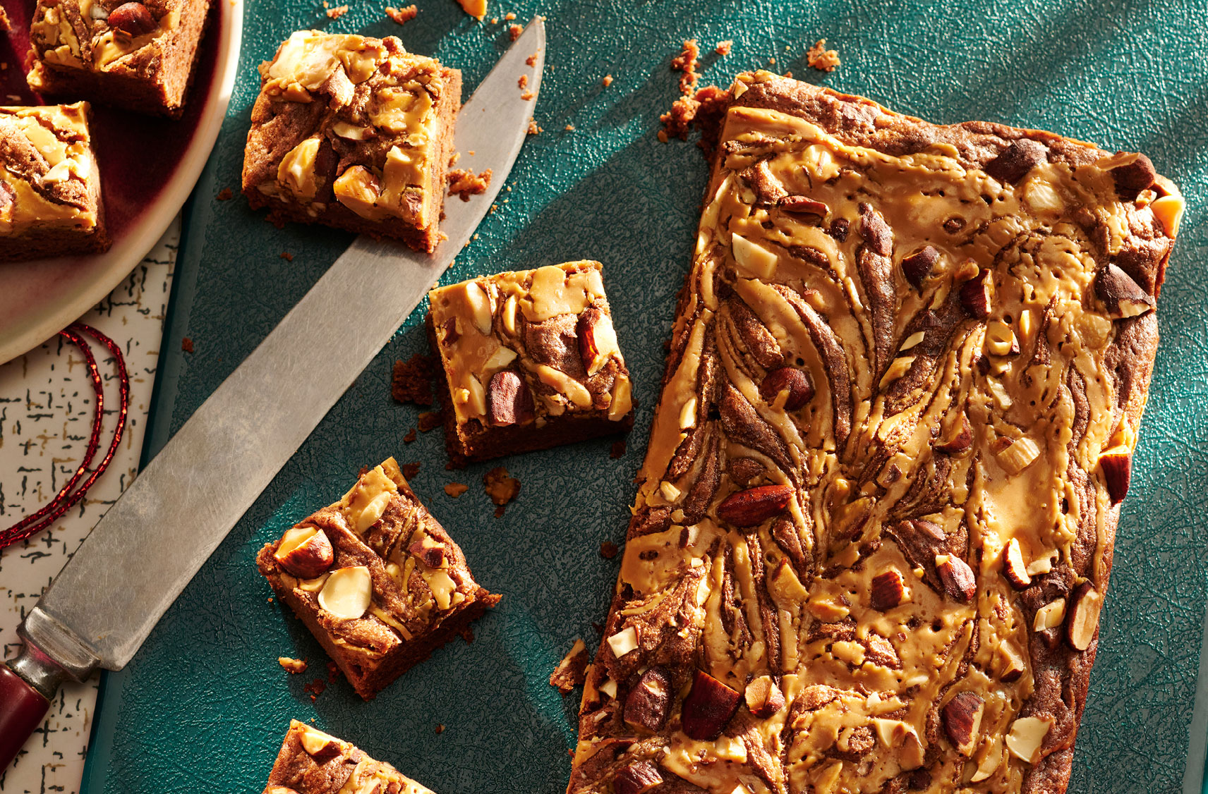 A cutting board with a marble slab brownie topped with tamari-flavoured Almonds with 4 portions cut on the side.
