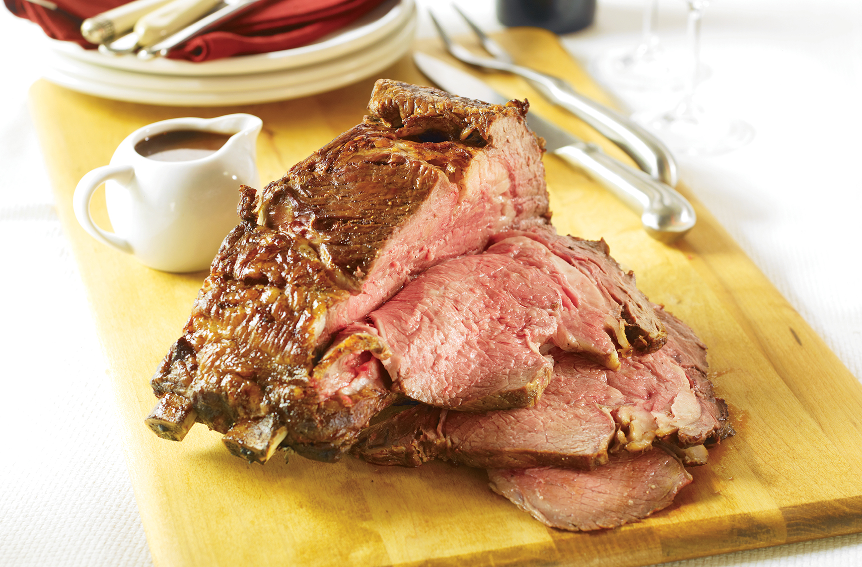 roast beef sliced up and placed on wooden cutting board for serving.  pan gravy placed in a small pouring dish on the side