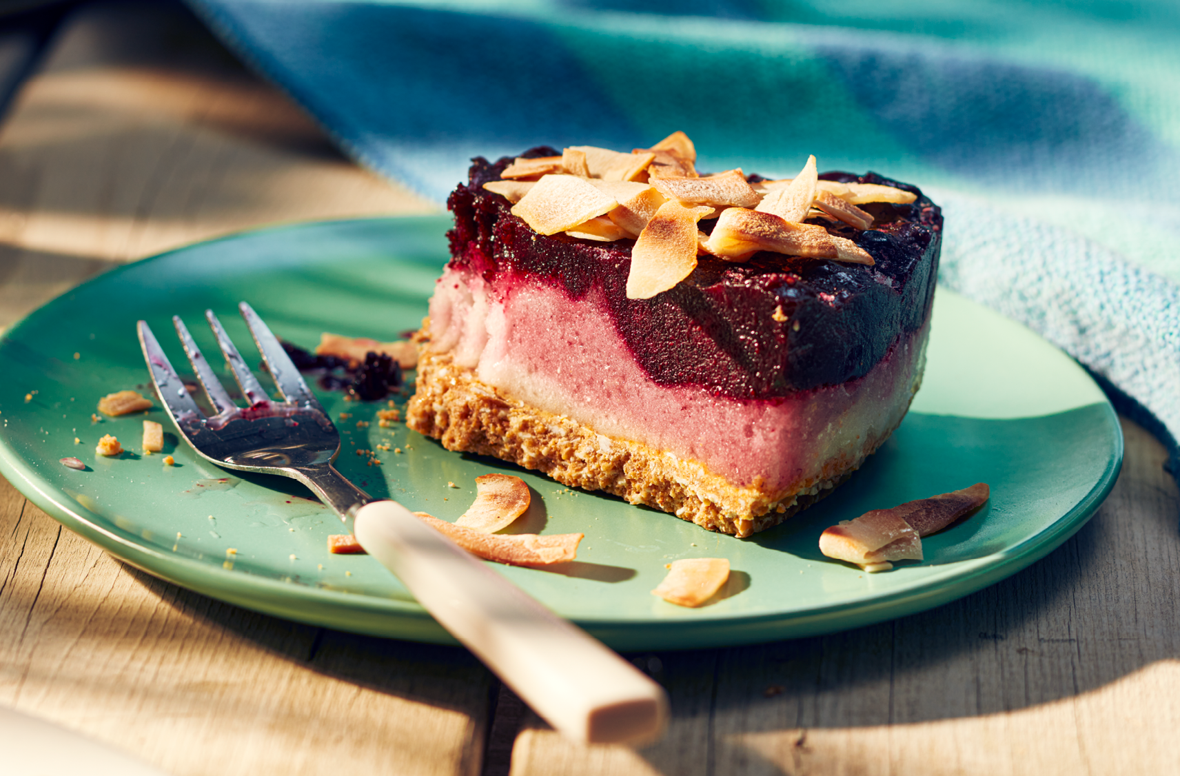 Une pointe de tarte au sorbet yuzu et bleuets garnie d'amandes effilées dont on a pris une bouchée sur une assiette.