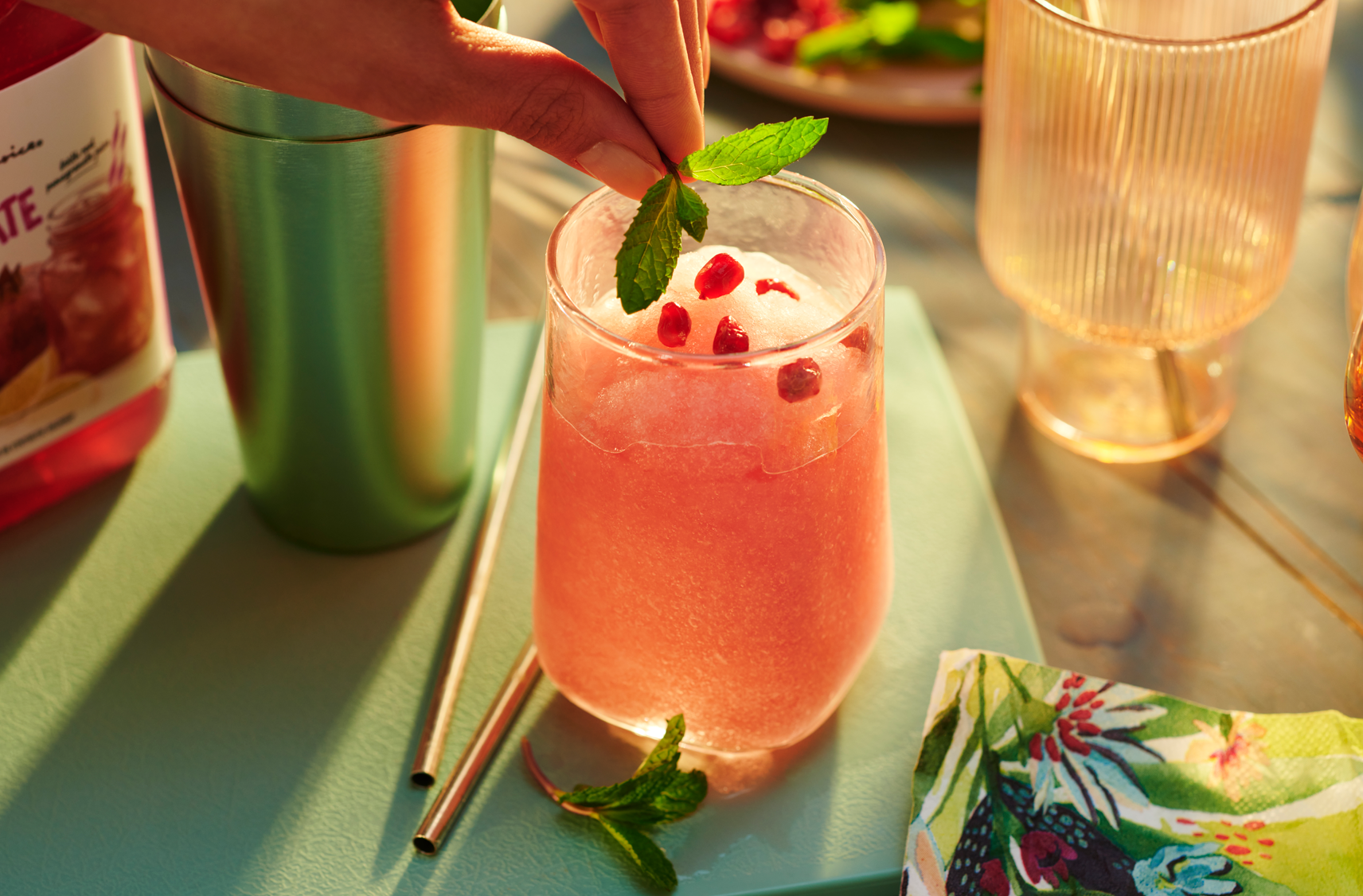 A hand putting mint leaves into a glass of pomegranate frose with arils on top.