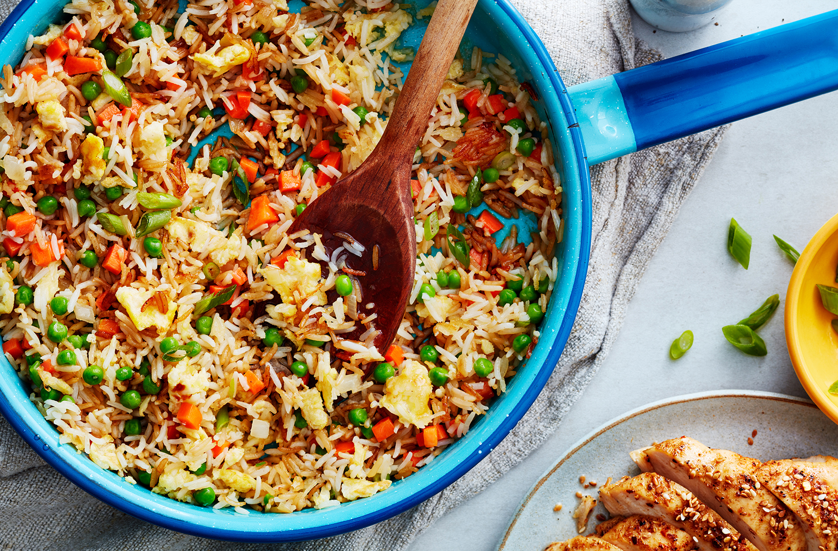 A spoon scoops up fried rice with diced carrot and peas from a blue skillet