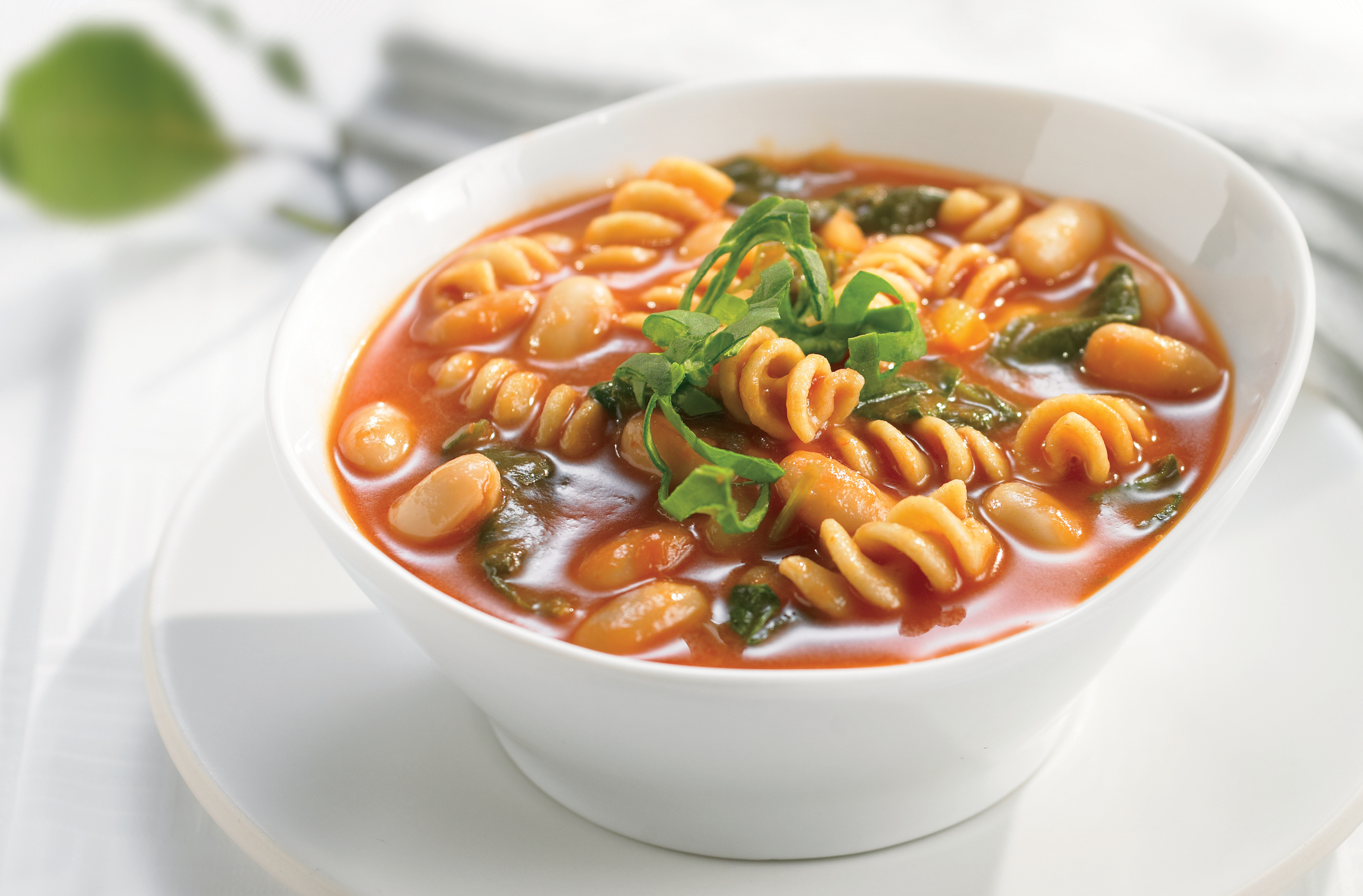 A bowl of rotini & kidney bean vegetable soup with onion, celery & spinach
