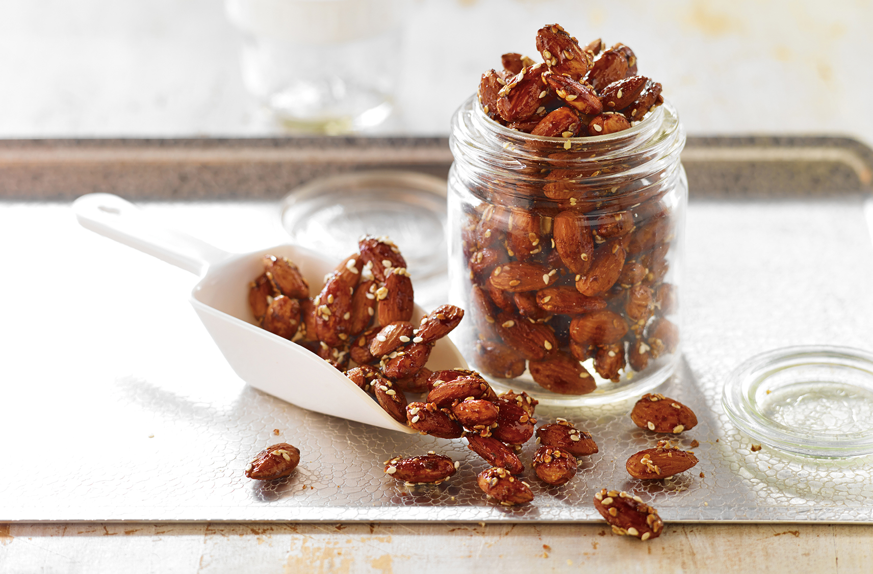Jar & scoop overflowing with almonds coated in honey & spices