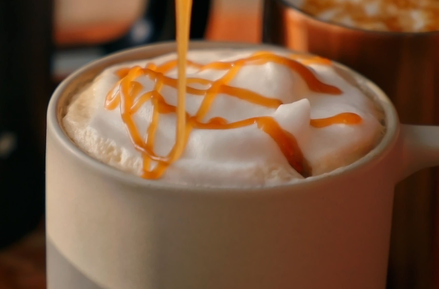Dulce de leche caramel is being drizzled onto a mug of a cookie butter flavoured latte