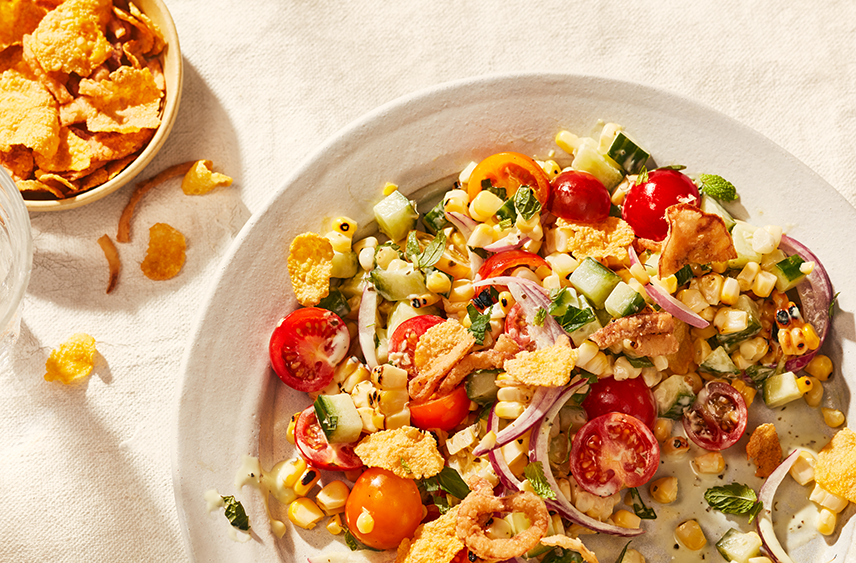 A plate containing a Corn and Tomato Salad with Crispy Corn Flakes on top and in a side dish.