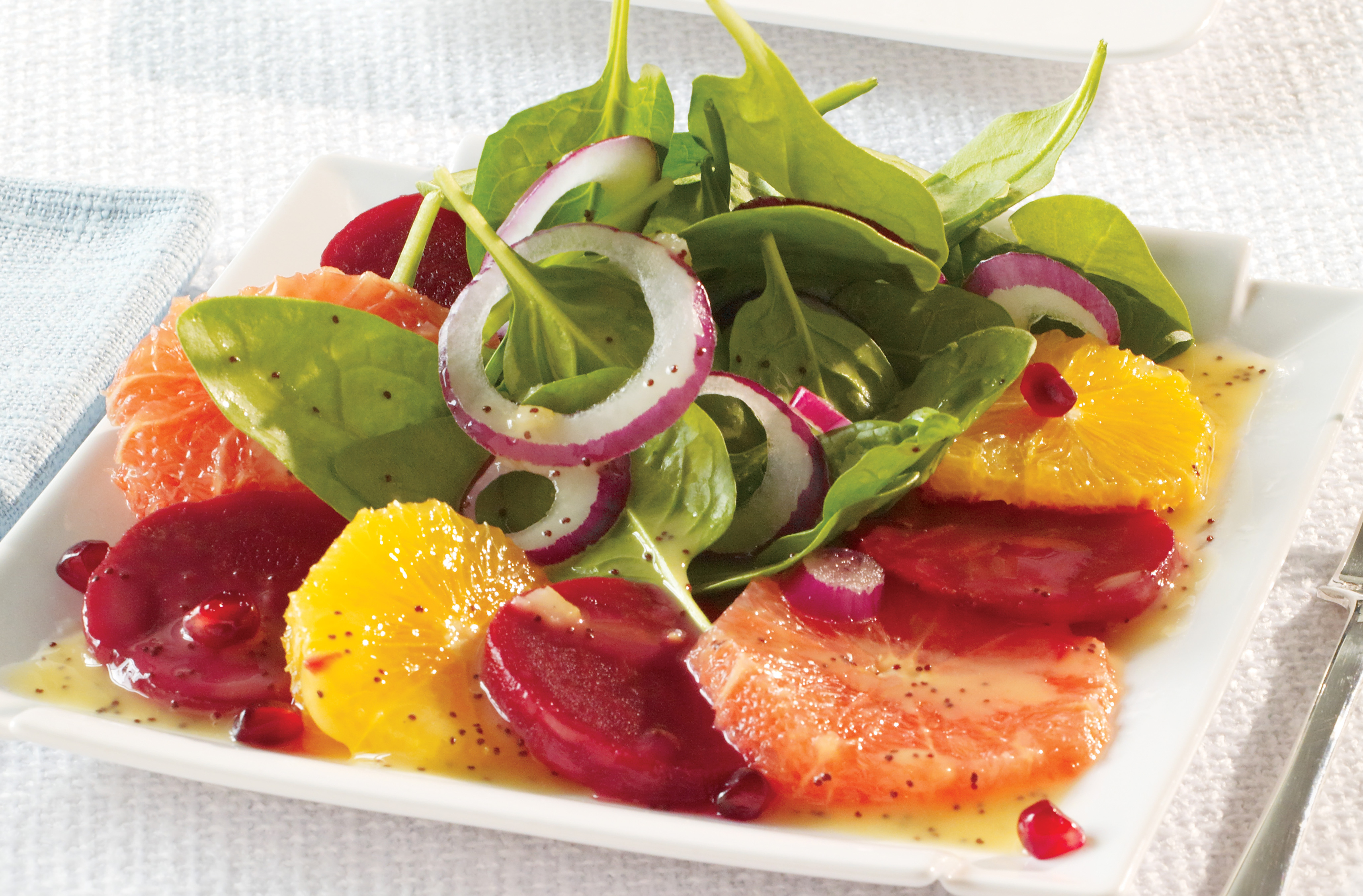 Plate of orange, red grapefruit & beet slices, topped with spinach & onion
