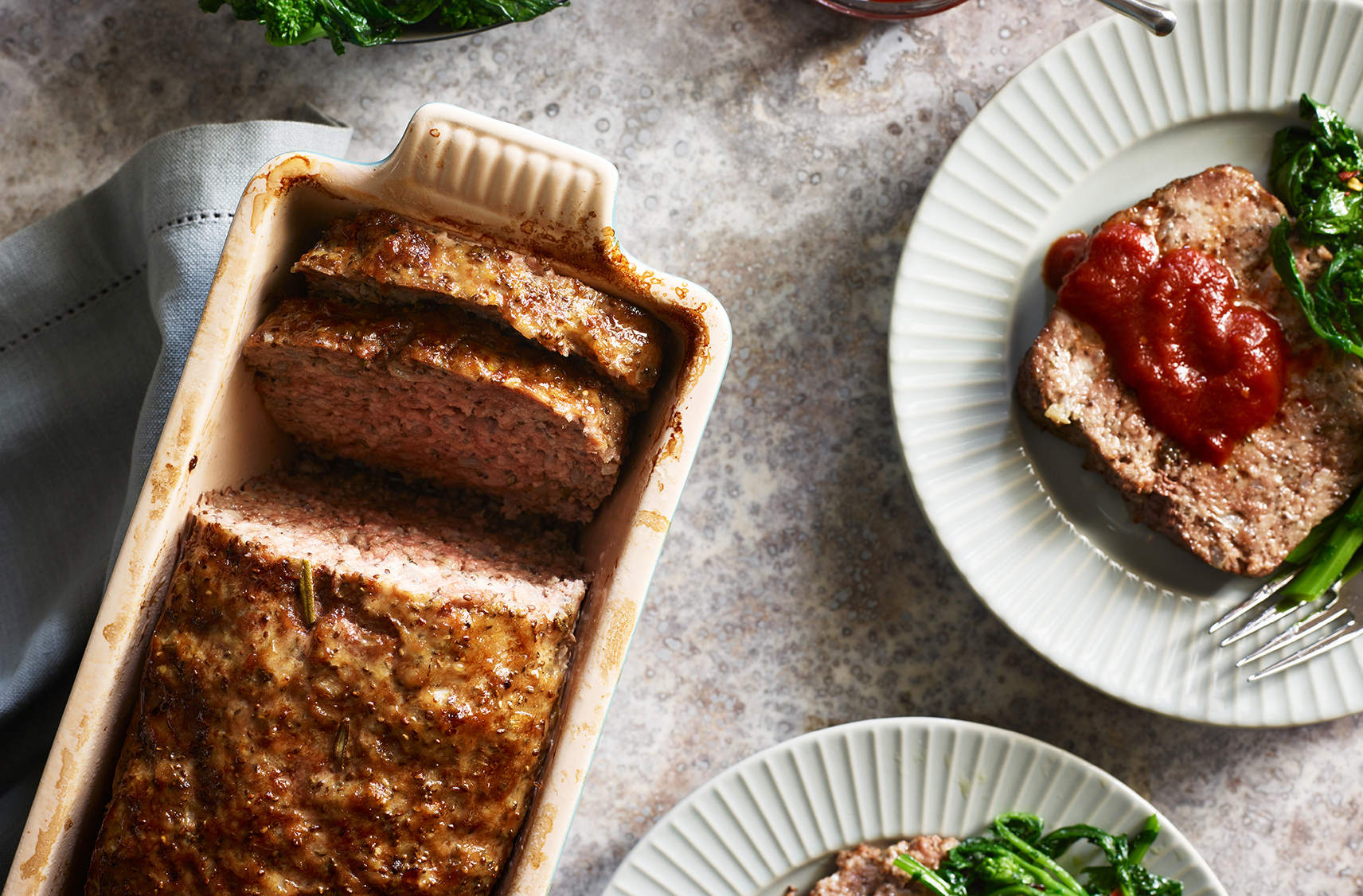 Sliced meatloaf in a dish with tomato sauce on the side 