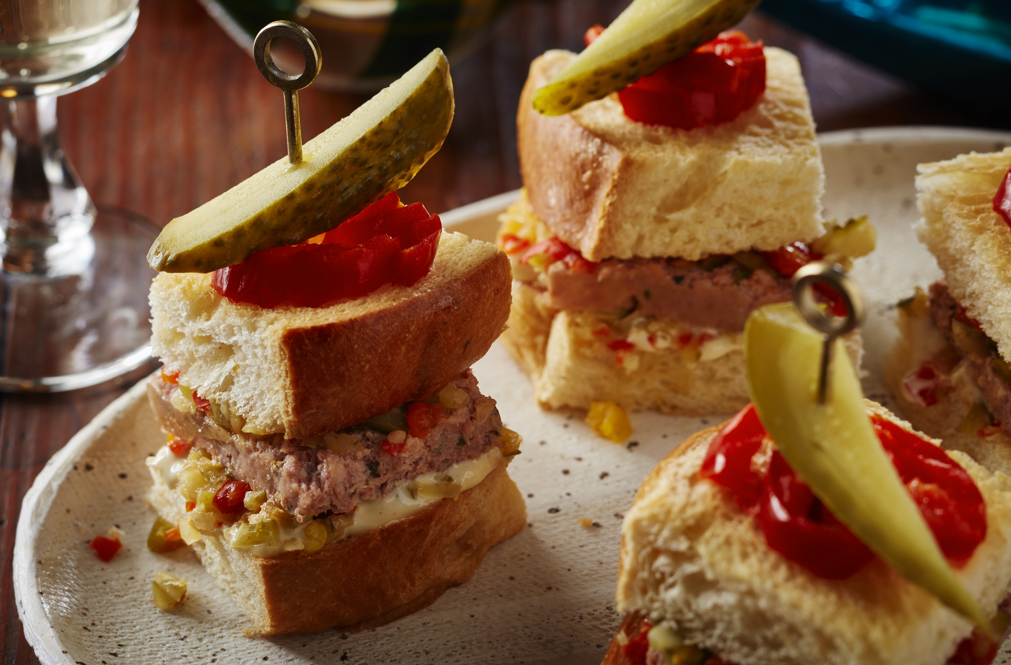 Pickles and hot peppers top mini sandwiches of pâté and relish on a platter
